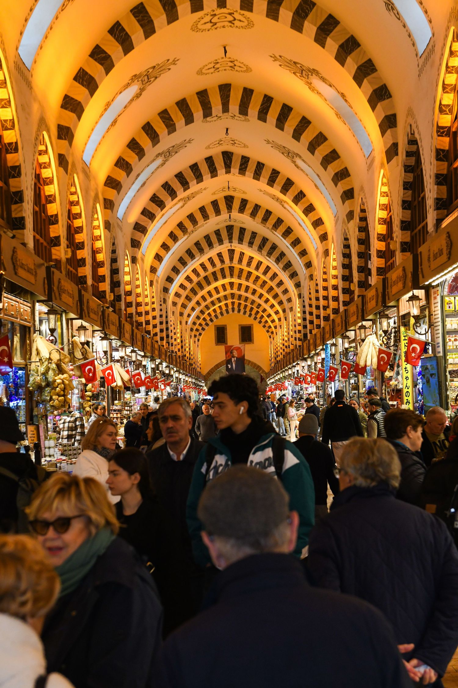 Crowded indoor bazaar with ornate arched ceilings illuminated in warm golden light.