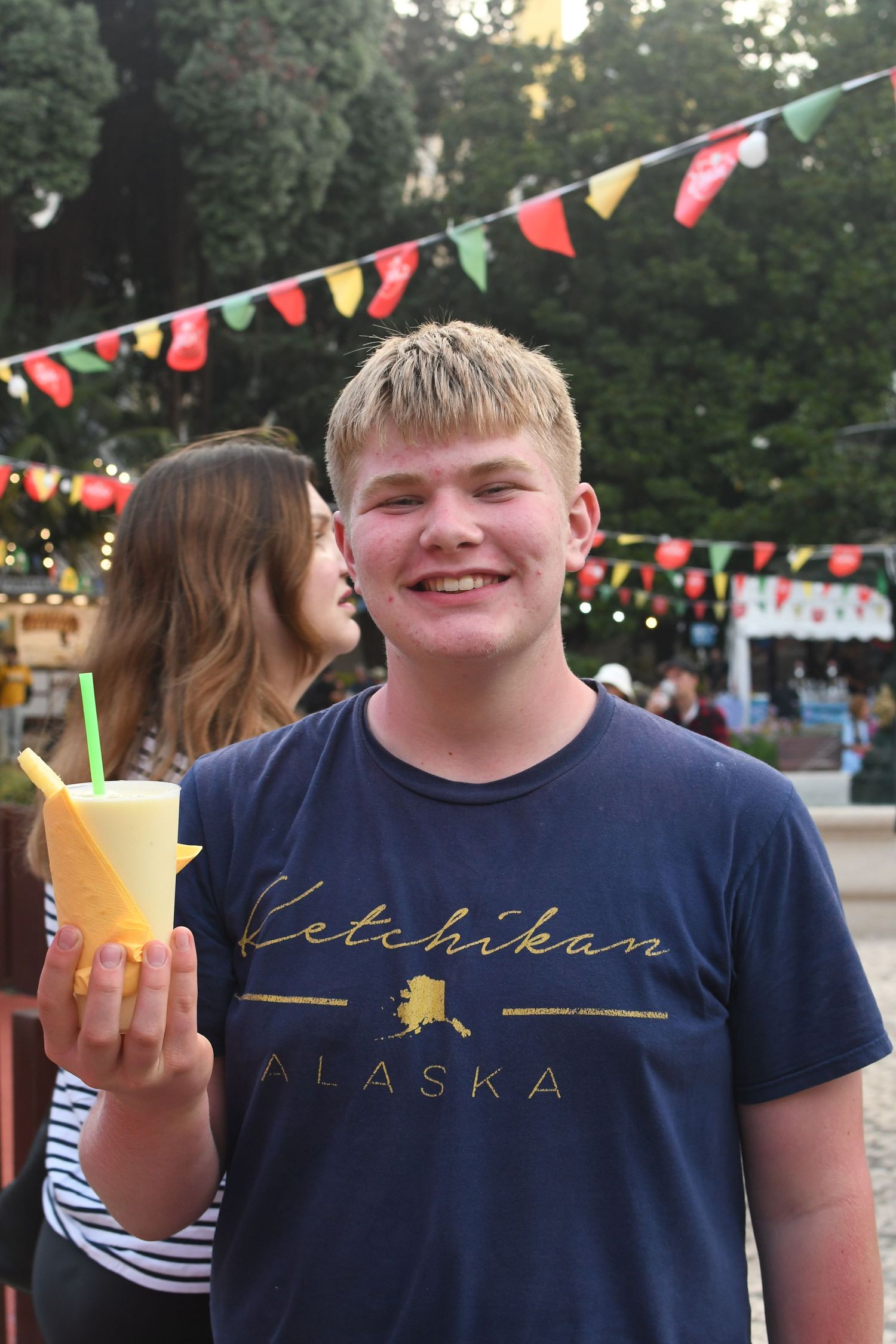 Tourist enjoying tropical drinks at an outdoor festival with colorful bunting flags.