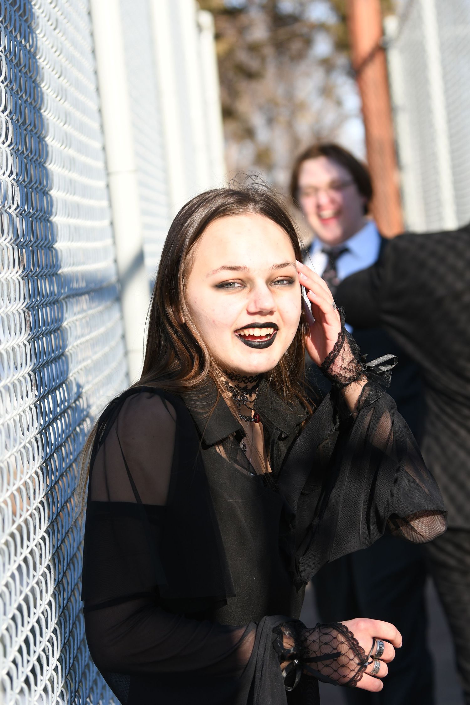 Gothic-styled portrait of person in black sheer top against chain link fence.