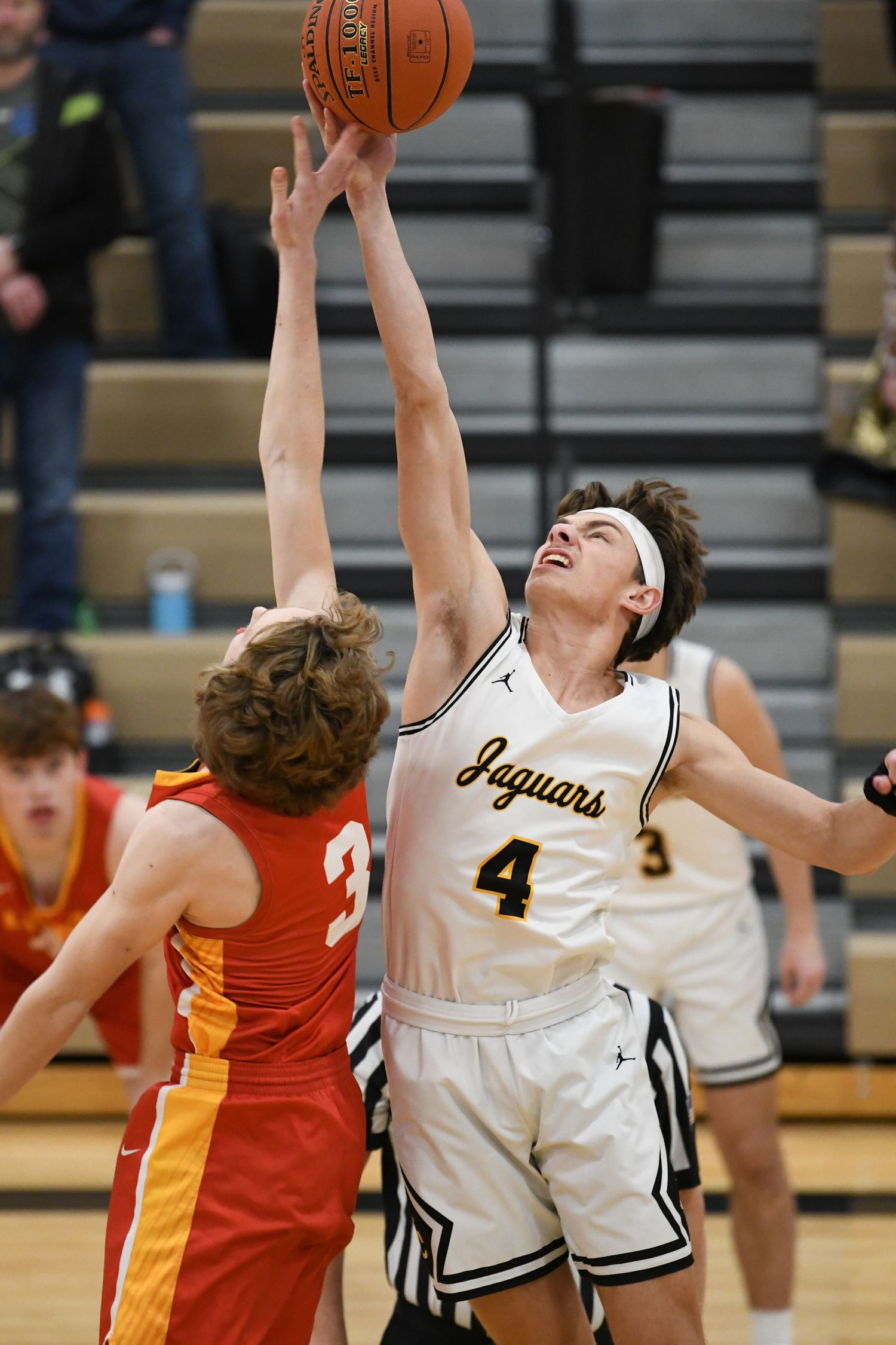 Two basketball players jump high battling for a rebound during competitive game action.