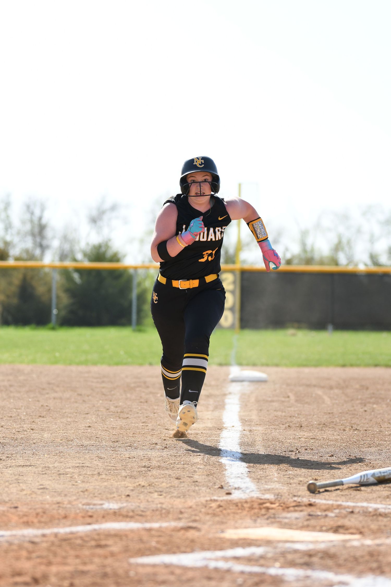 Softball player in black uniform slides into home plate during close play.