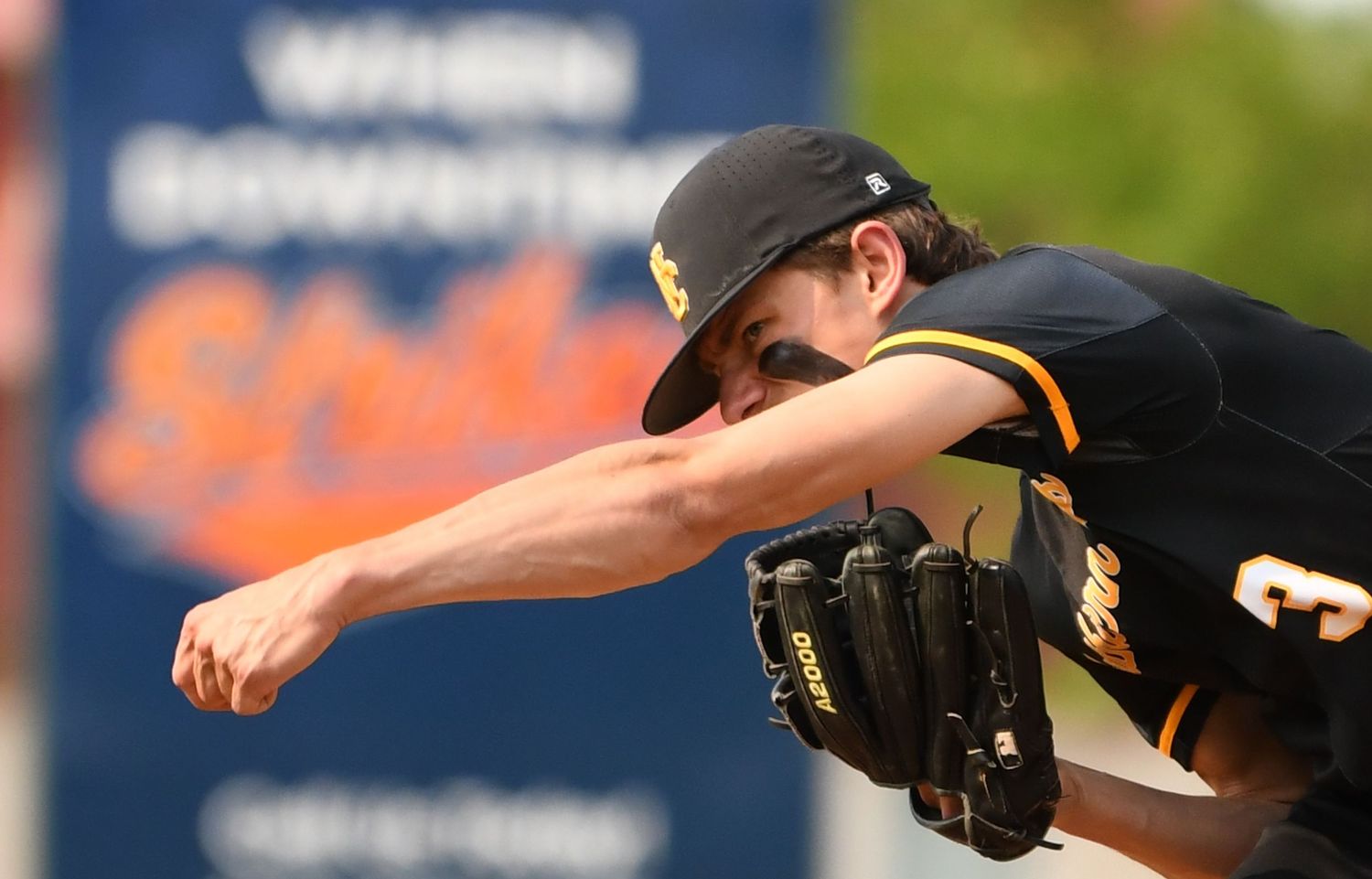 Baseball pitcher in mid-delivery motion wearing black uniform against blurred background.