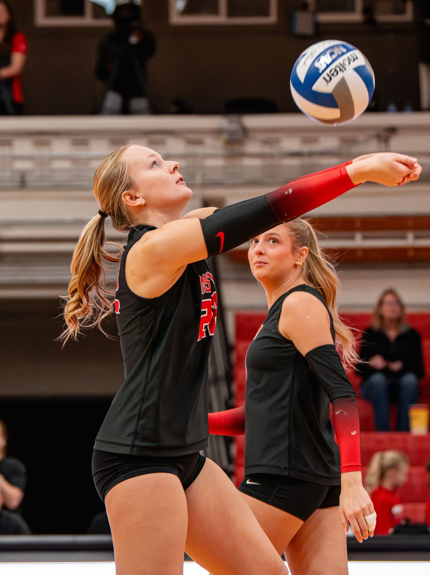 Volleyball players in black uniforms prepare to set the ball during an intense match on the court.
