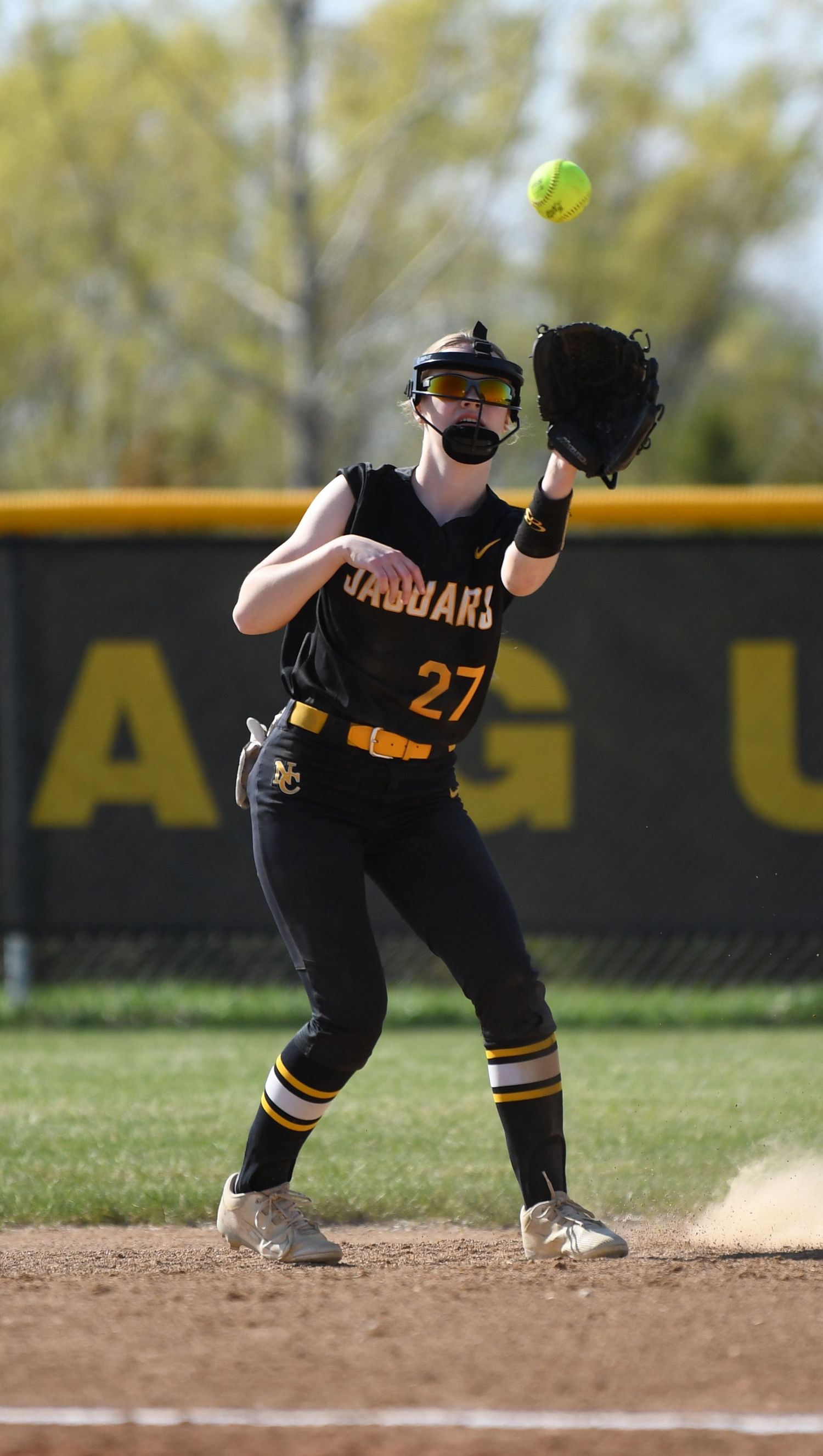 Infielder in black Jaguars uniform prepares to field ground ball during softball game.