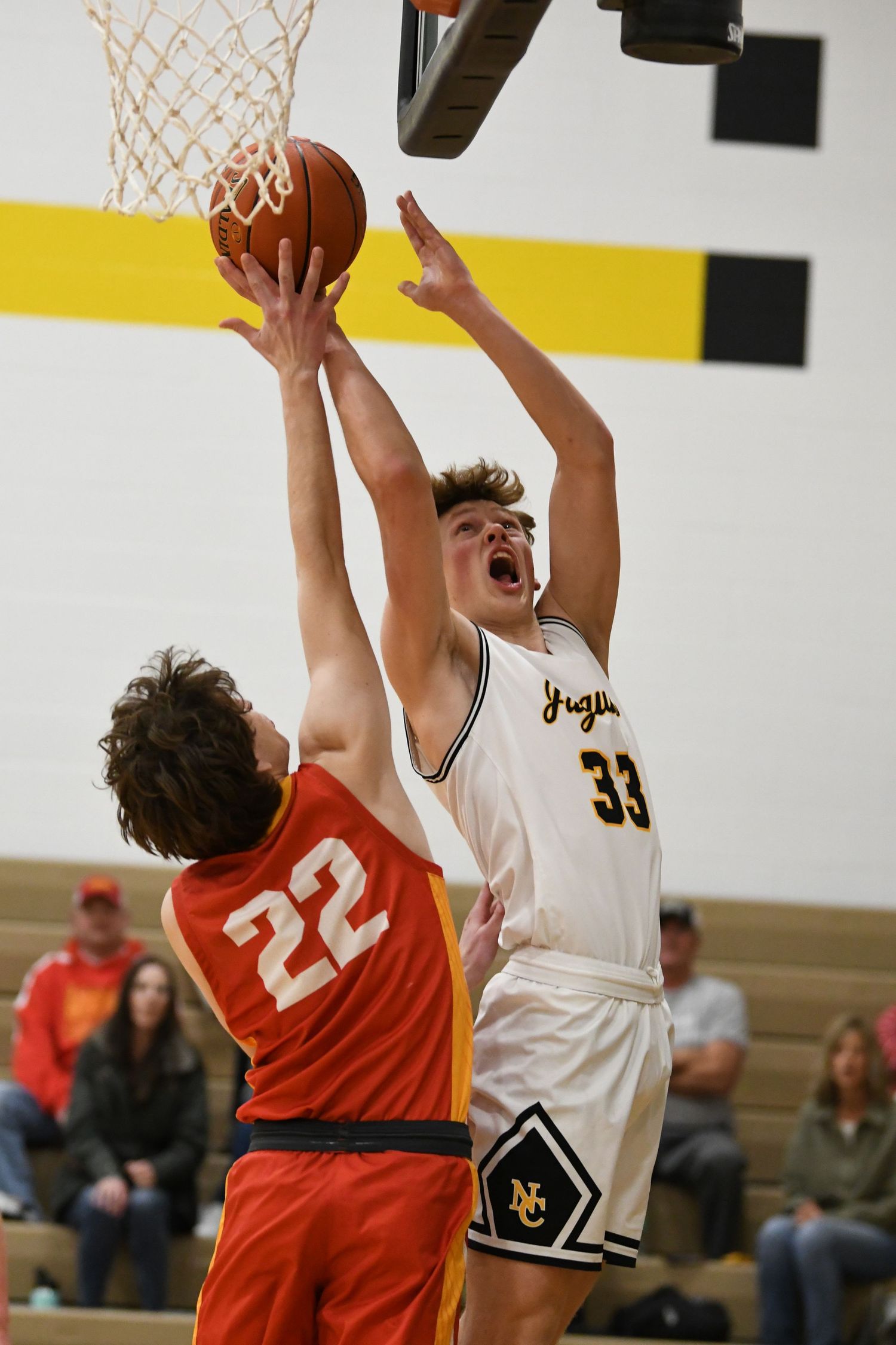 Basketball players from opposing teams leap for the ball near the basket during intense gameplay.