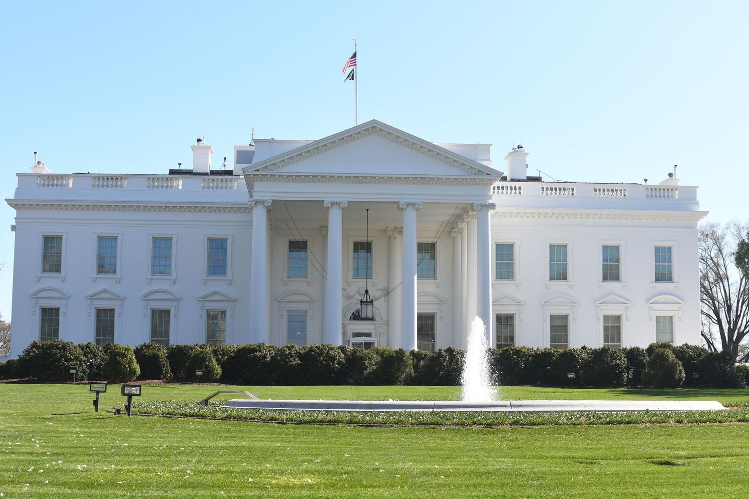 Panoramic view of the White House exterior with manicured lawns and fountains on a sunny day.