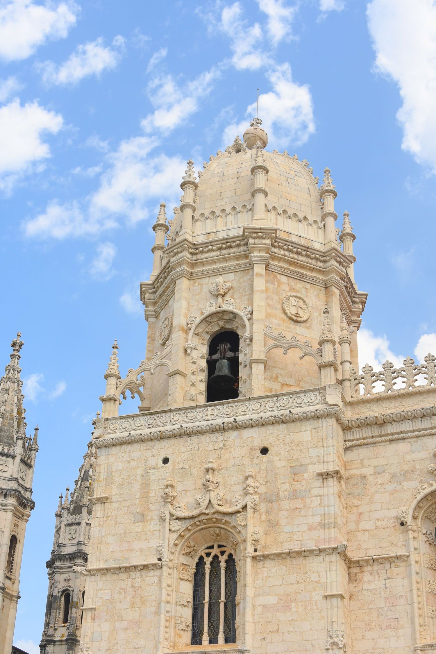 Ornate Gothic bell tower of a cathedral against bright blue sky with white clouds.