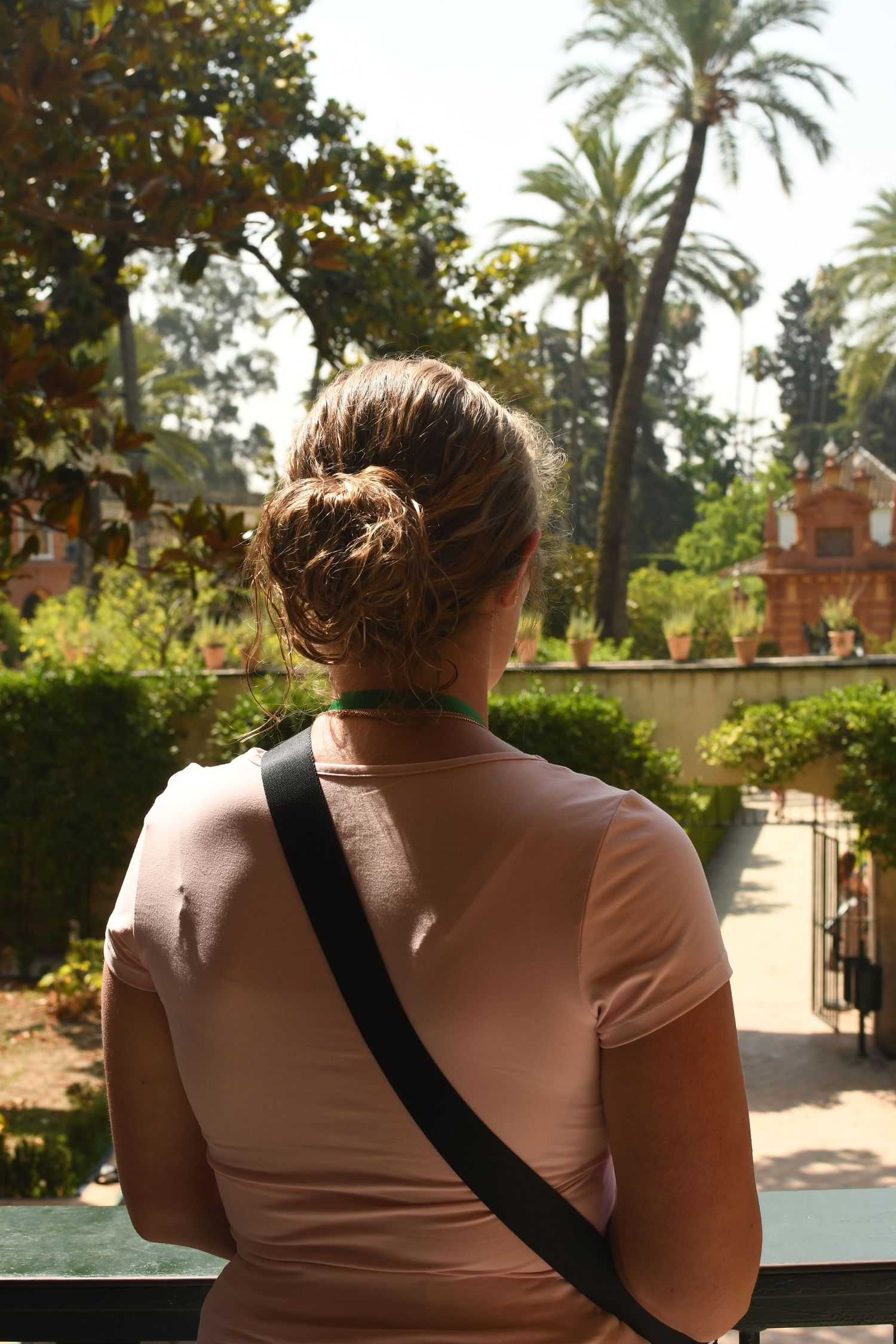 Back view of tourist looking out over historic garden with palm trees and Spanish architecture.