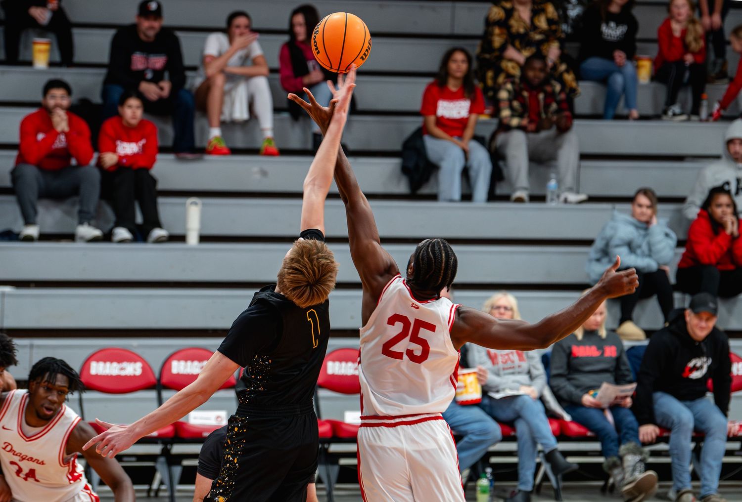 Basketball players leap for a rebound during an intense game in a crowded gymnasium.