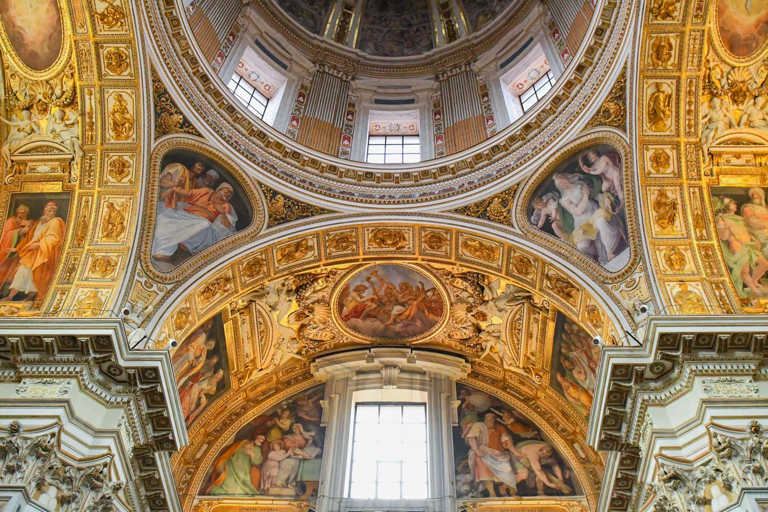 Ornate baroque church ceiling with gilded decorations and painted frescoes around central dome.