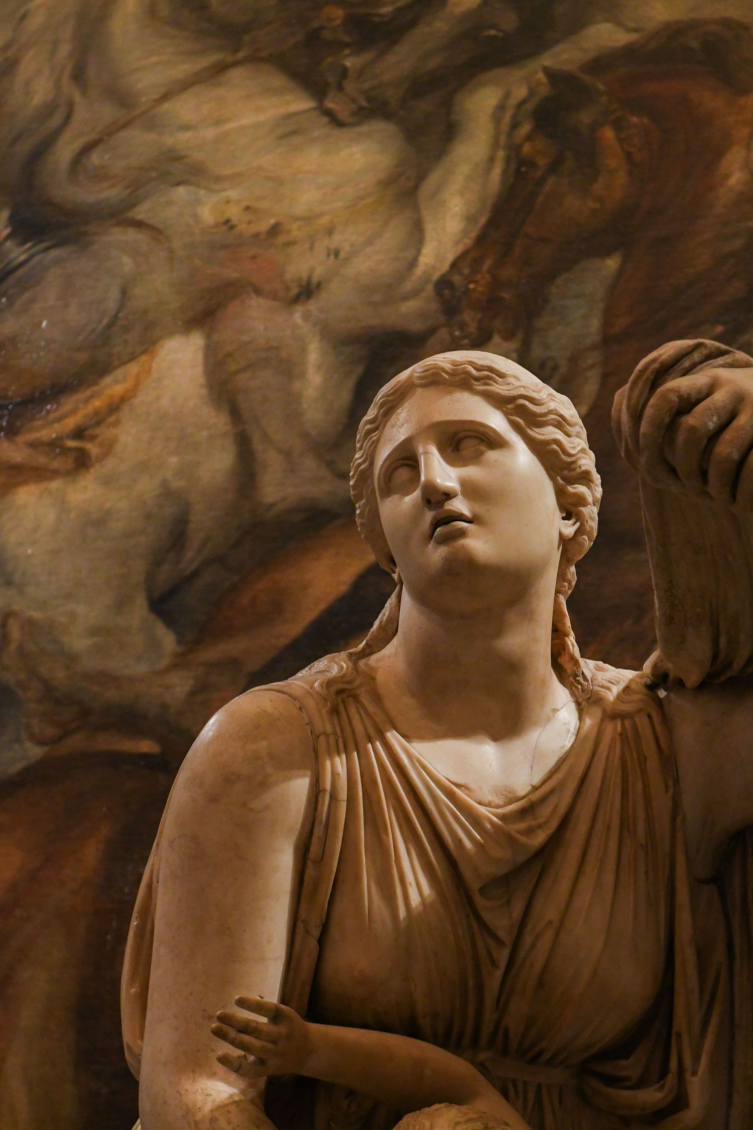 Classical marble sculpture of a draped figure with upturned gaze in dramatic lighting.