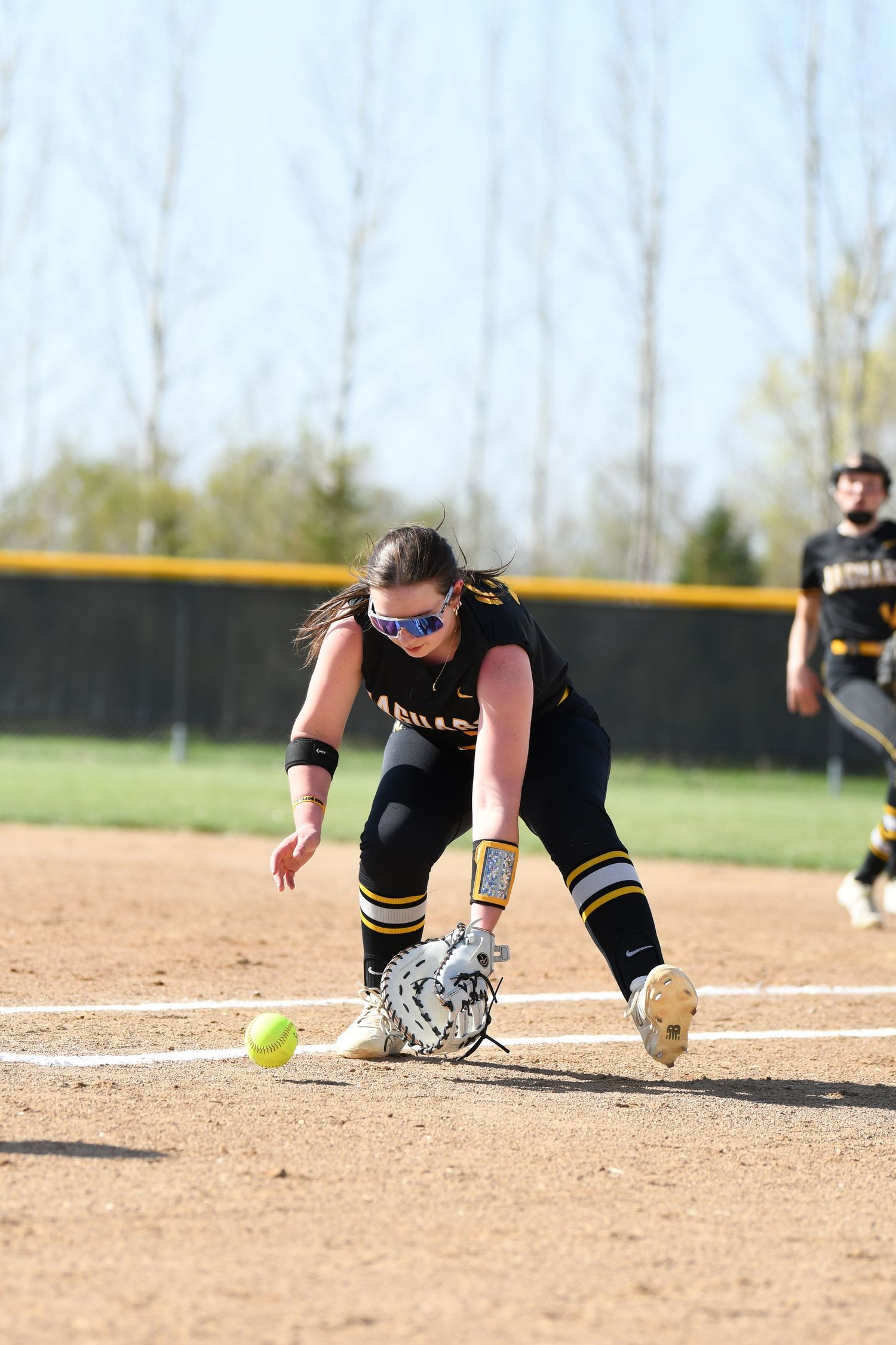 Softball infielder dives for ground ball during defensive play on dirt field.