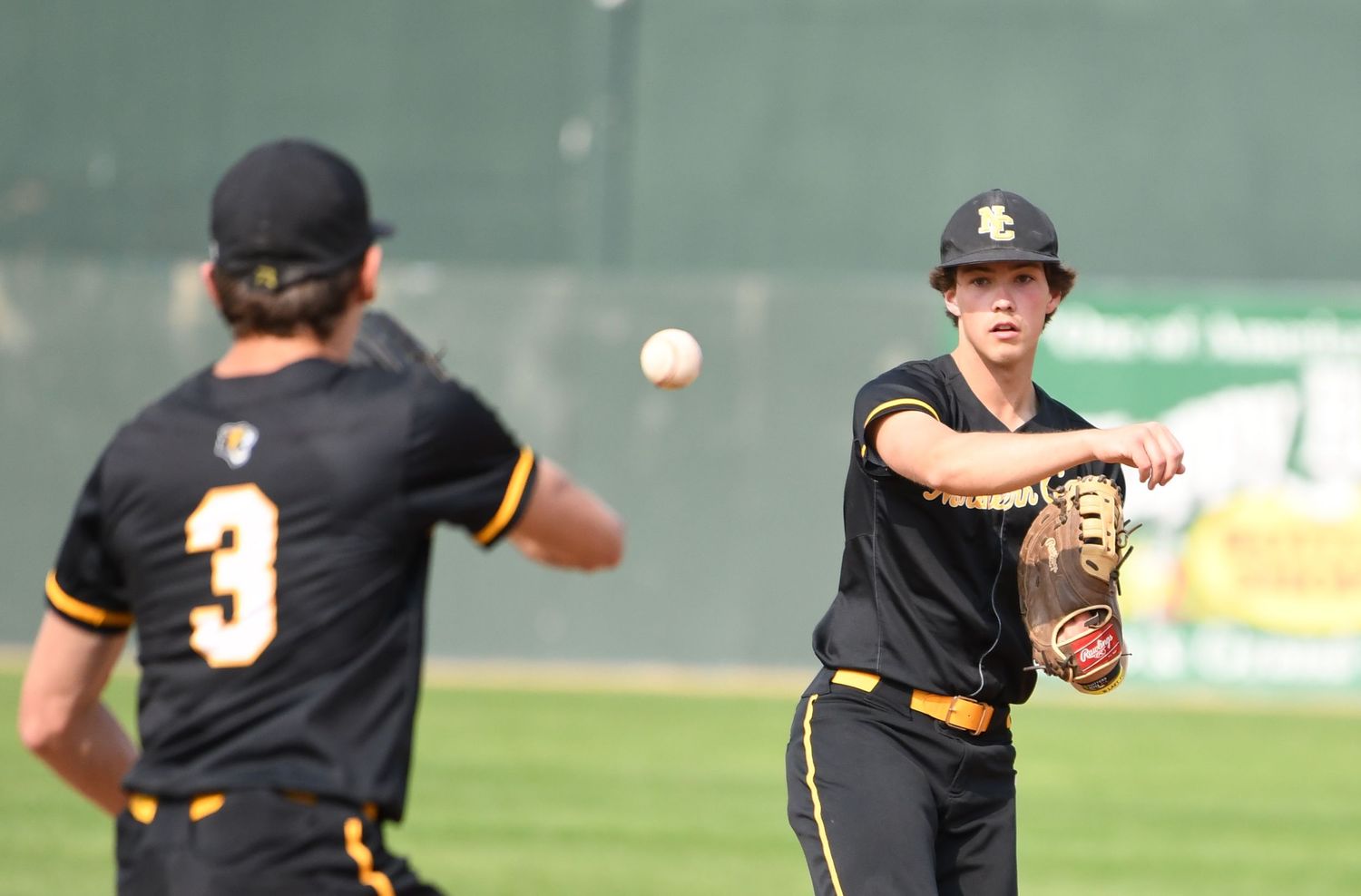 Baseball players in black uniforms practicing pitching drills on a green field.