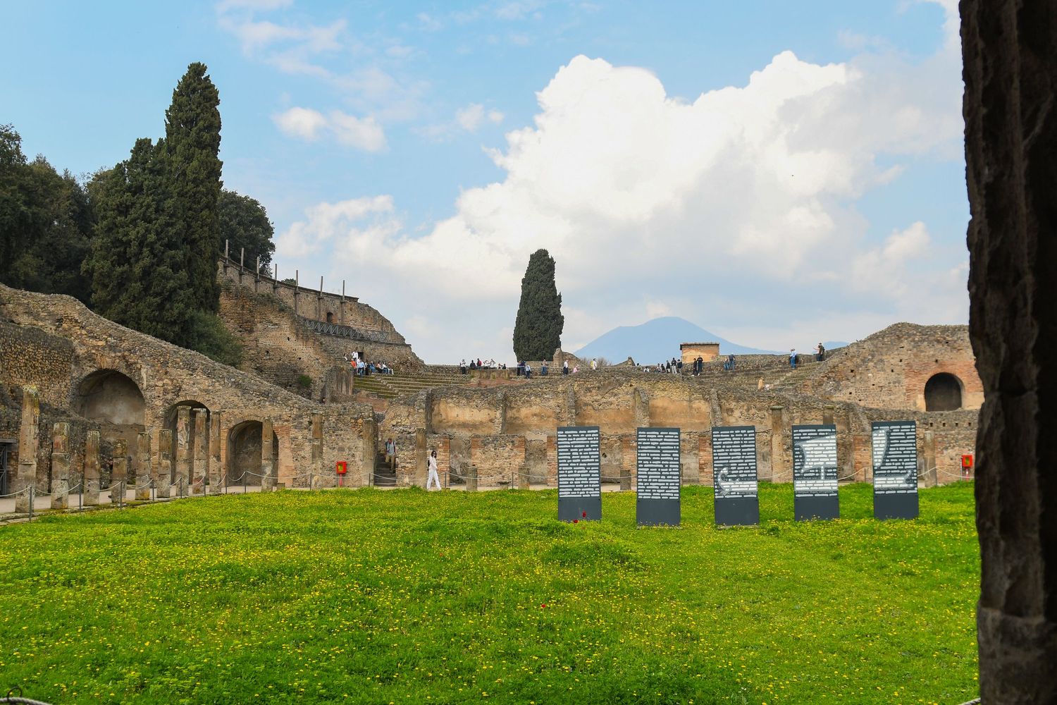 Ancient Roman ruins and stone columns against blue sky with cypress trees.