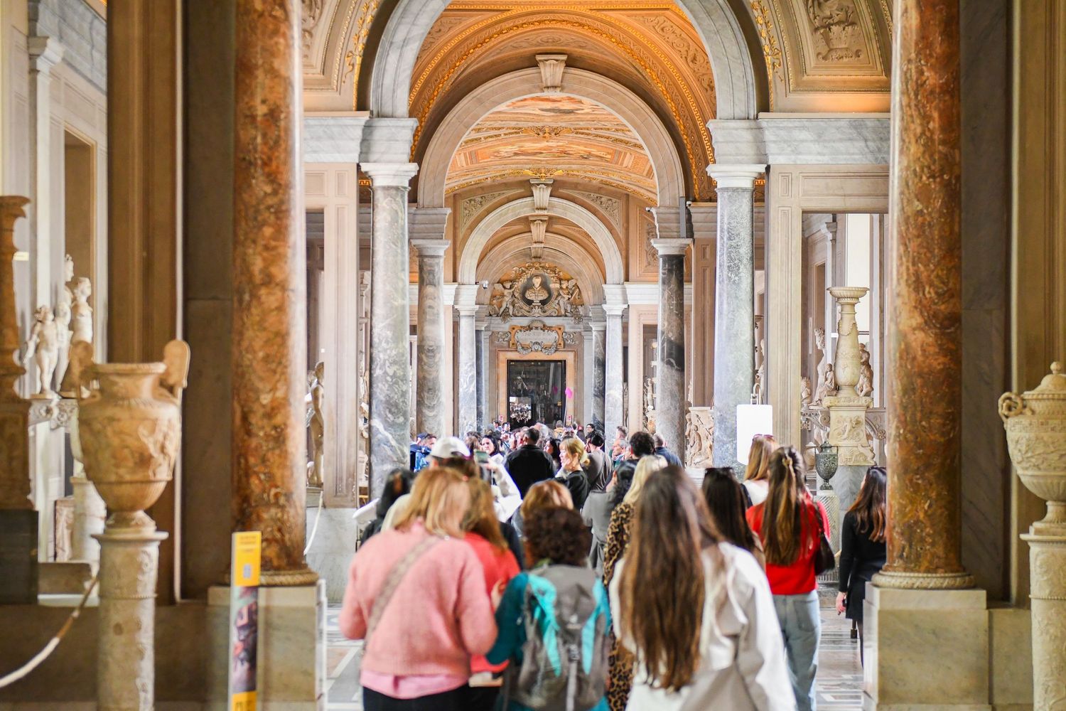Long corridor with arched colonnade and classical statues in historic museum gallery.