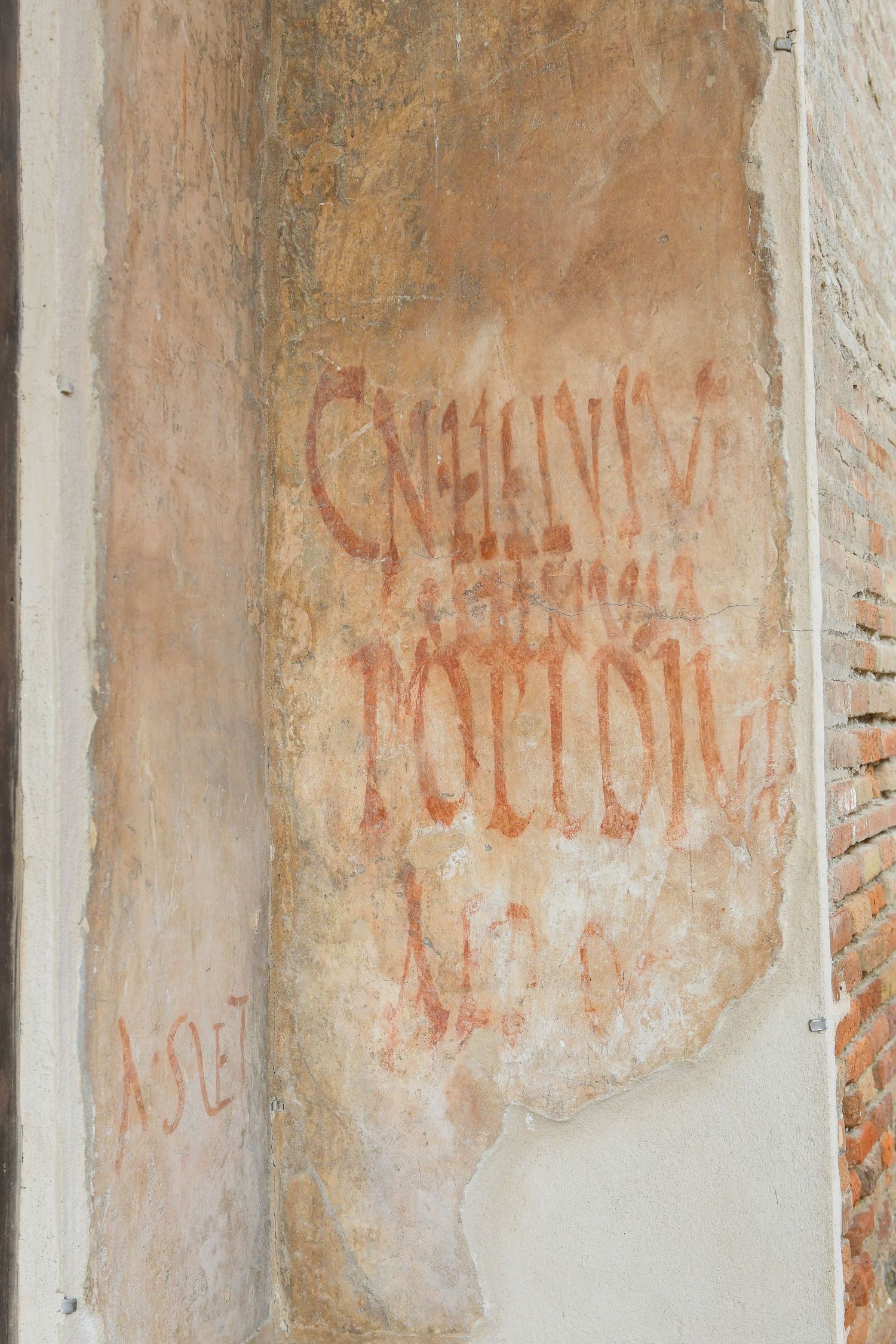 Ancient Roman wall with faded red inscriptions and graffiti visible on weathered plaster surface.