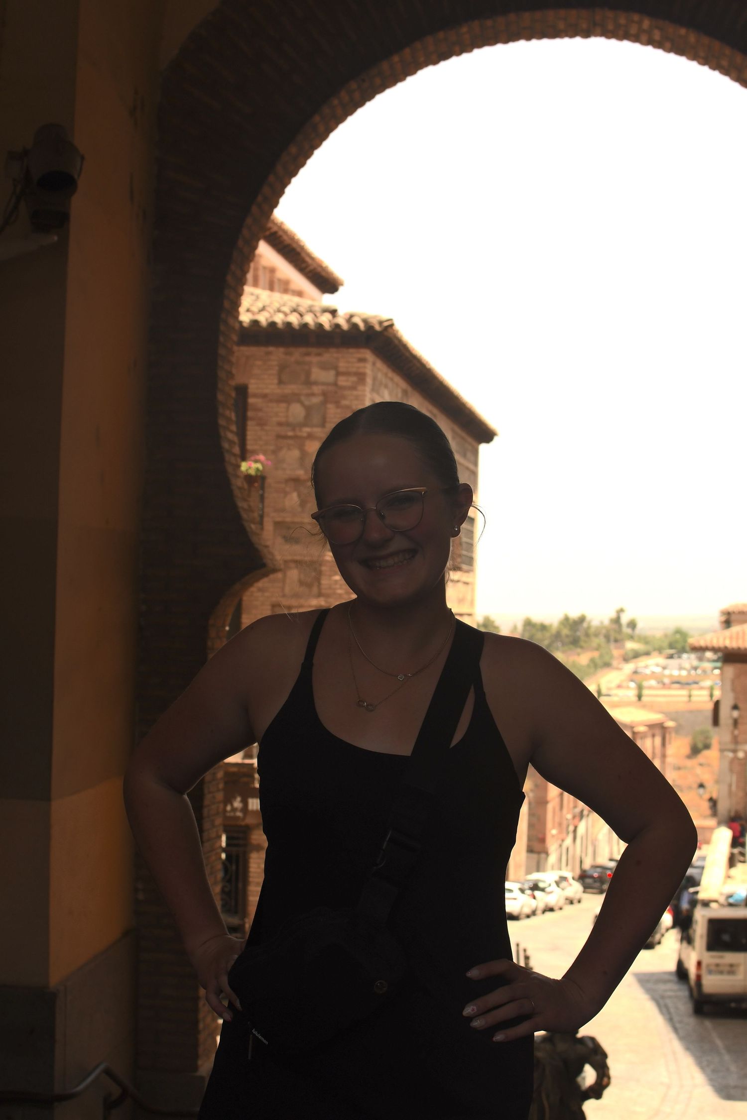 Tourist poses in stone archway overlooking Mediterranean town at sunset.