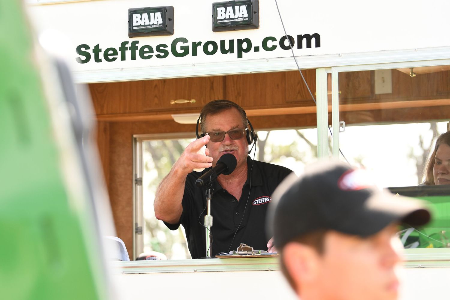 A group of people tour agricultural equipment inside a large warehouse facility with SteffesGroup.com signage.