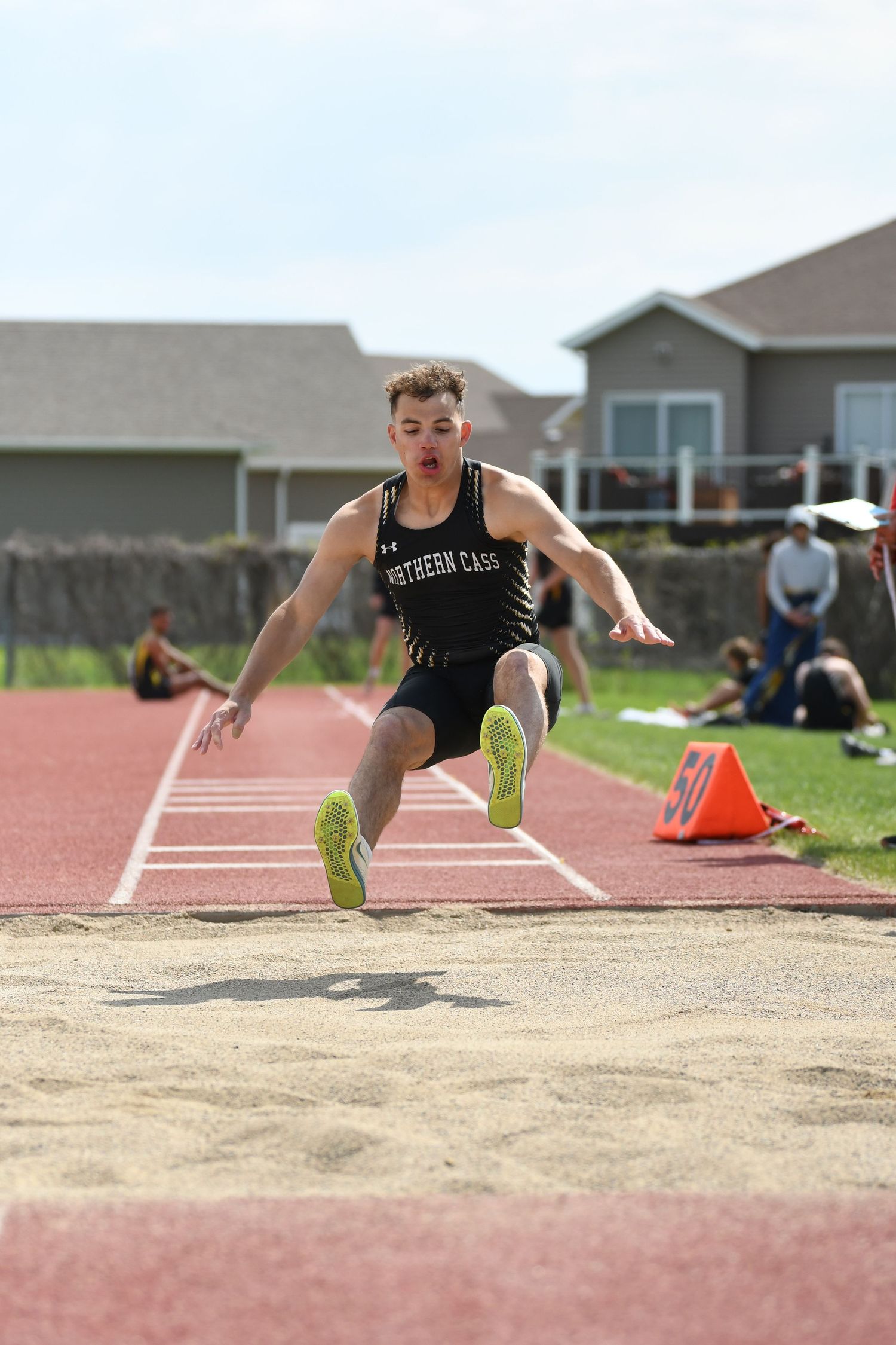 Long jumper soars through air before landing in sand pit during track meet.