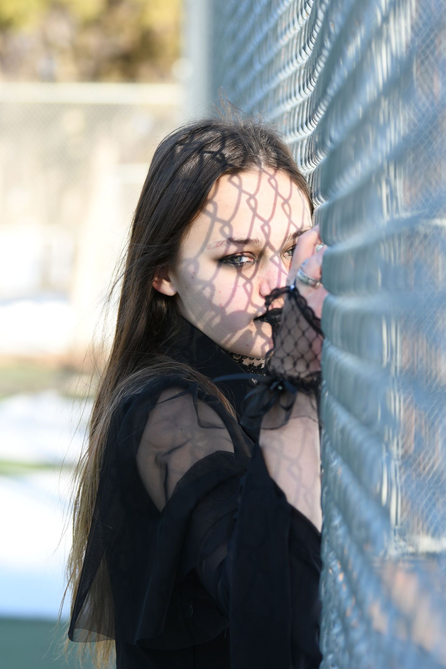 Artistic portrait with fence shadow pattern casting across dark-dressed figure.