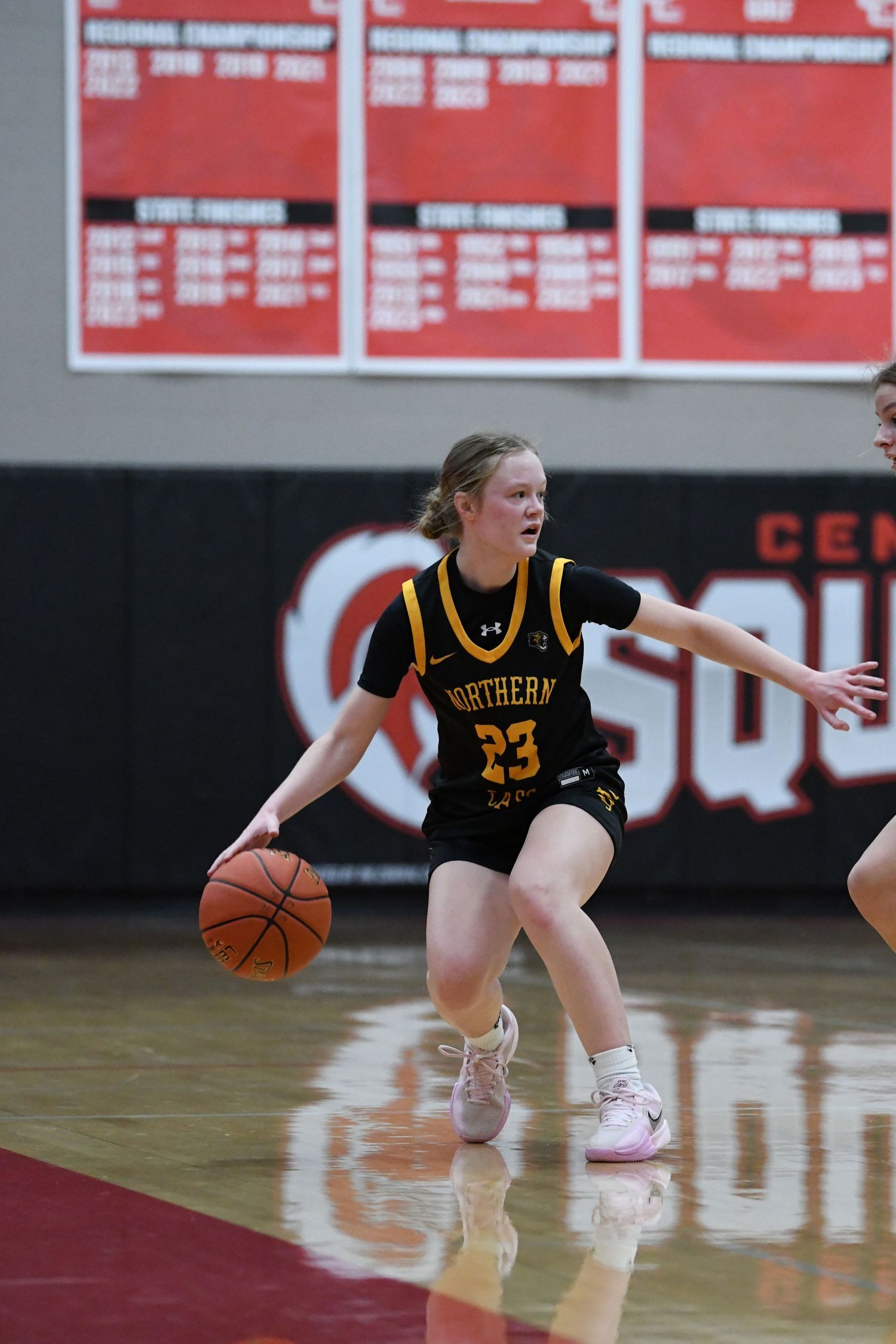 Basketball player in black Northern uniform dribbles during game with red background.