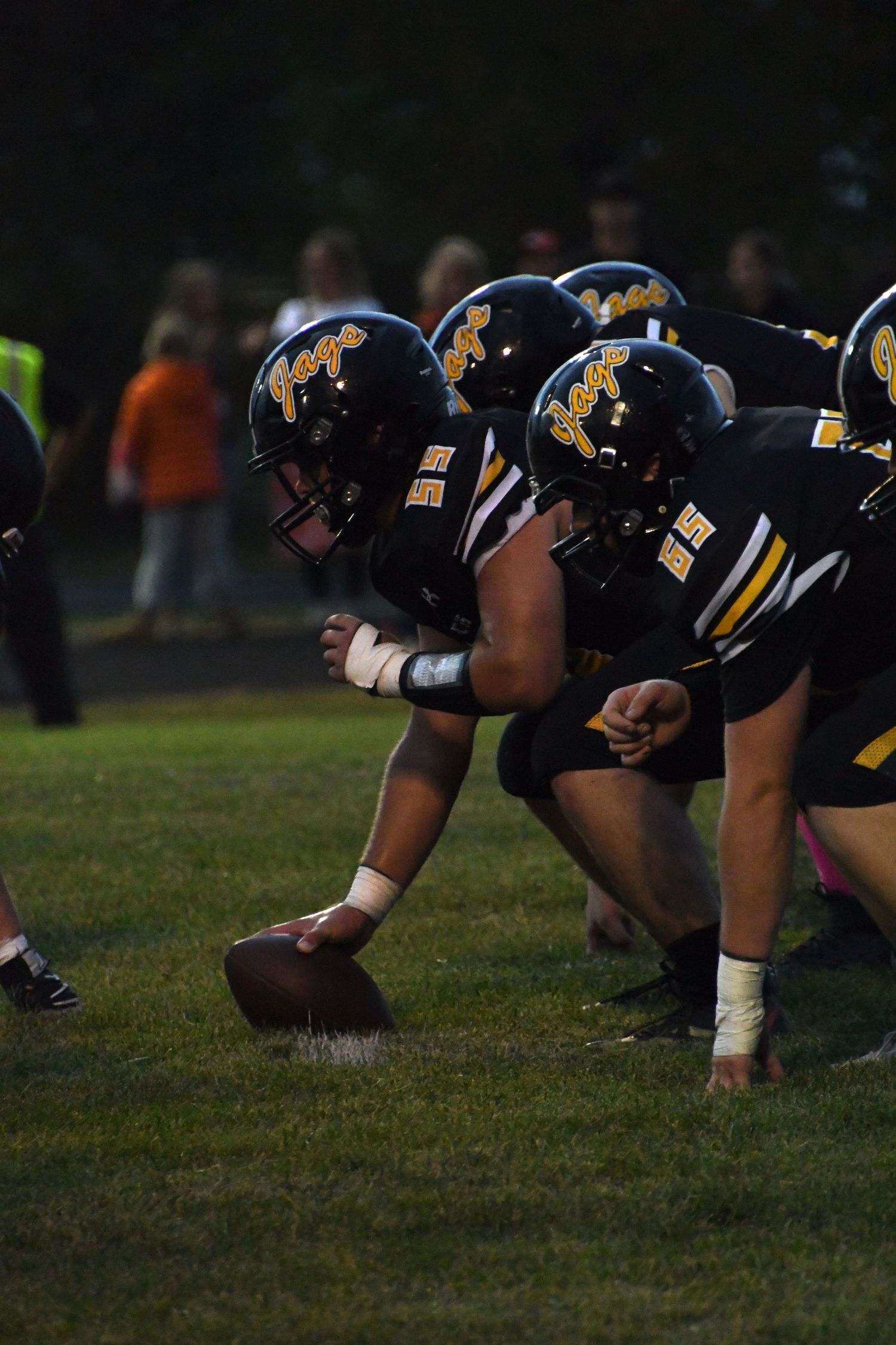 Football offensive line crouches in formation wearing black helmets with gold logos.