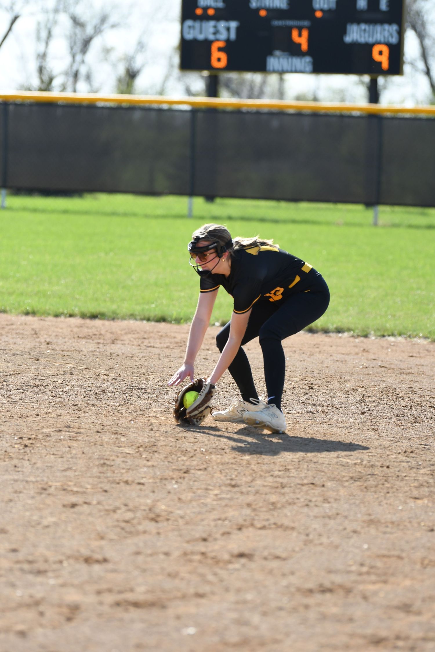 Infielder in black and gold uniform fielding ground ball during softball game.