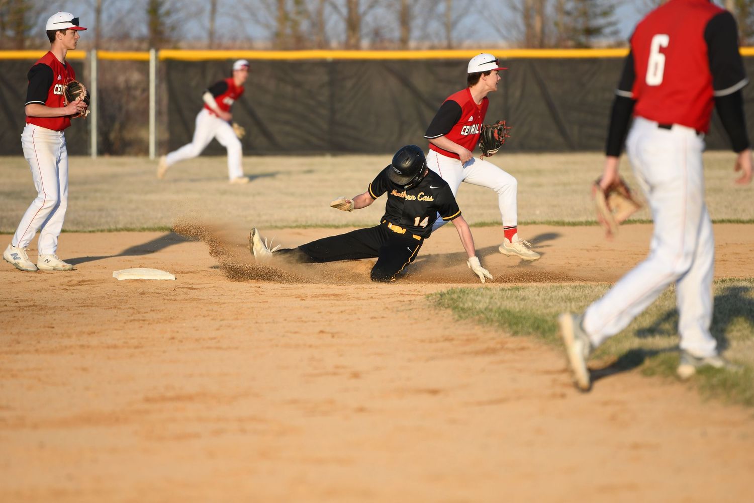 Baseball player in black uniform slides into base during competitive game.