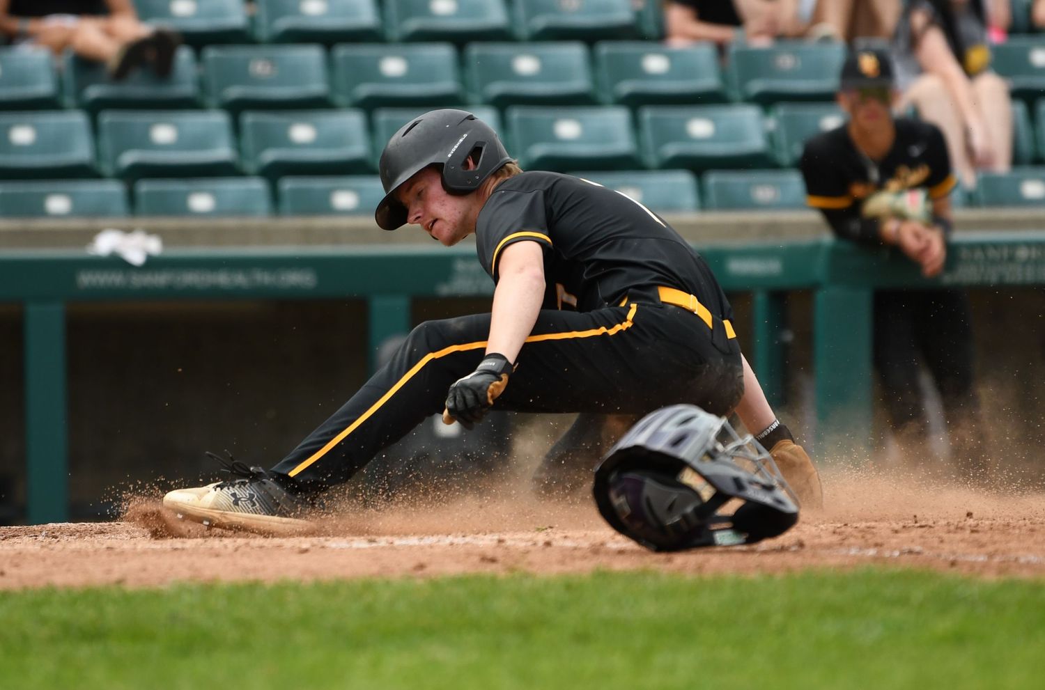 Baseball player in black uniform crouches near home plate during game action.