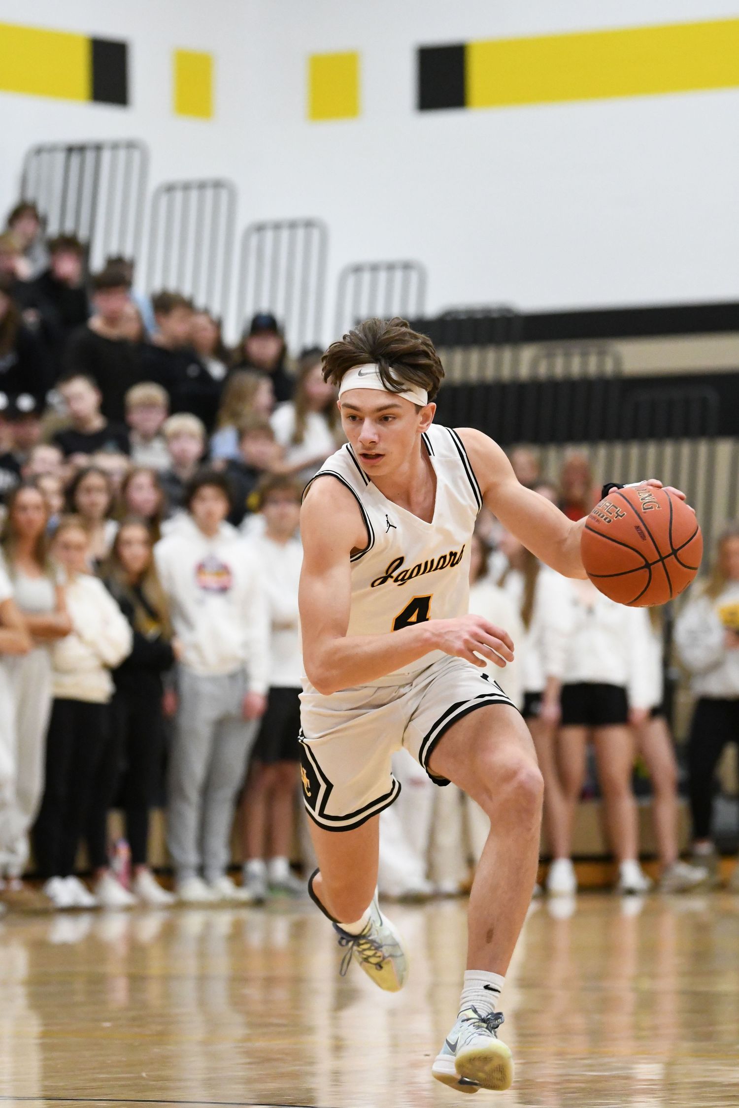 Basketball player in white jersey drives down court during fast break play.