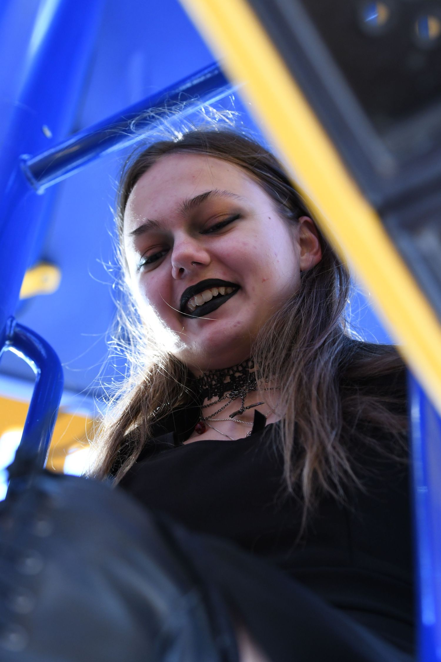 Low angle view of a person with dark lipstick and long hair against a blue and yellow background.