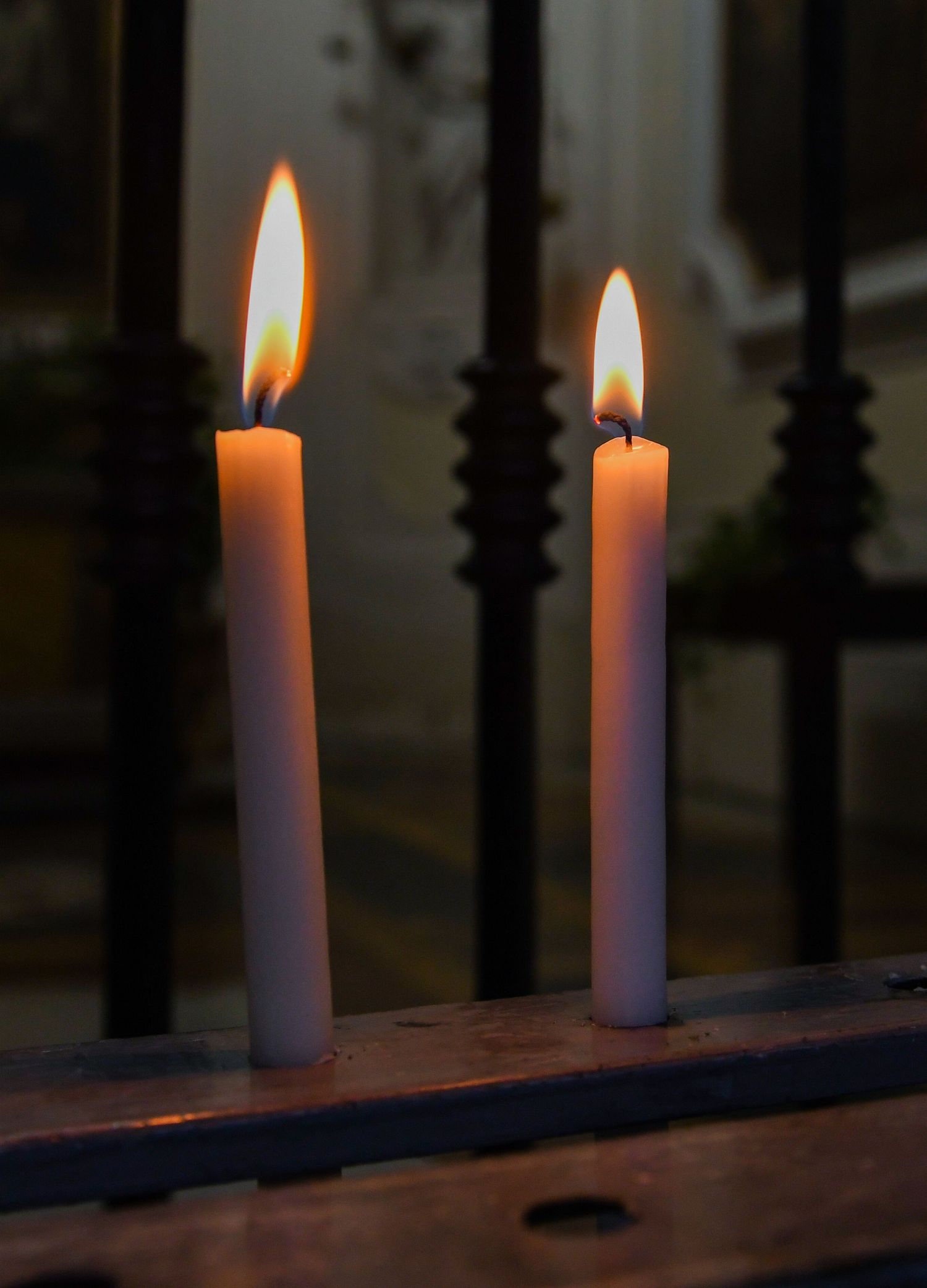Two white candles burning with glowing flames against a dark background.