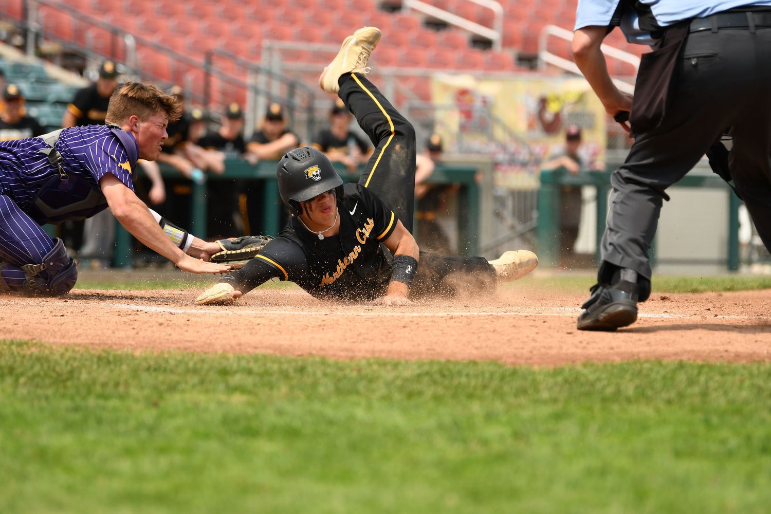 A dramatic play at home plate shows a baserunner sliding as the catcher attempts to make the tag.