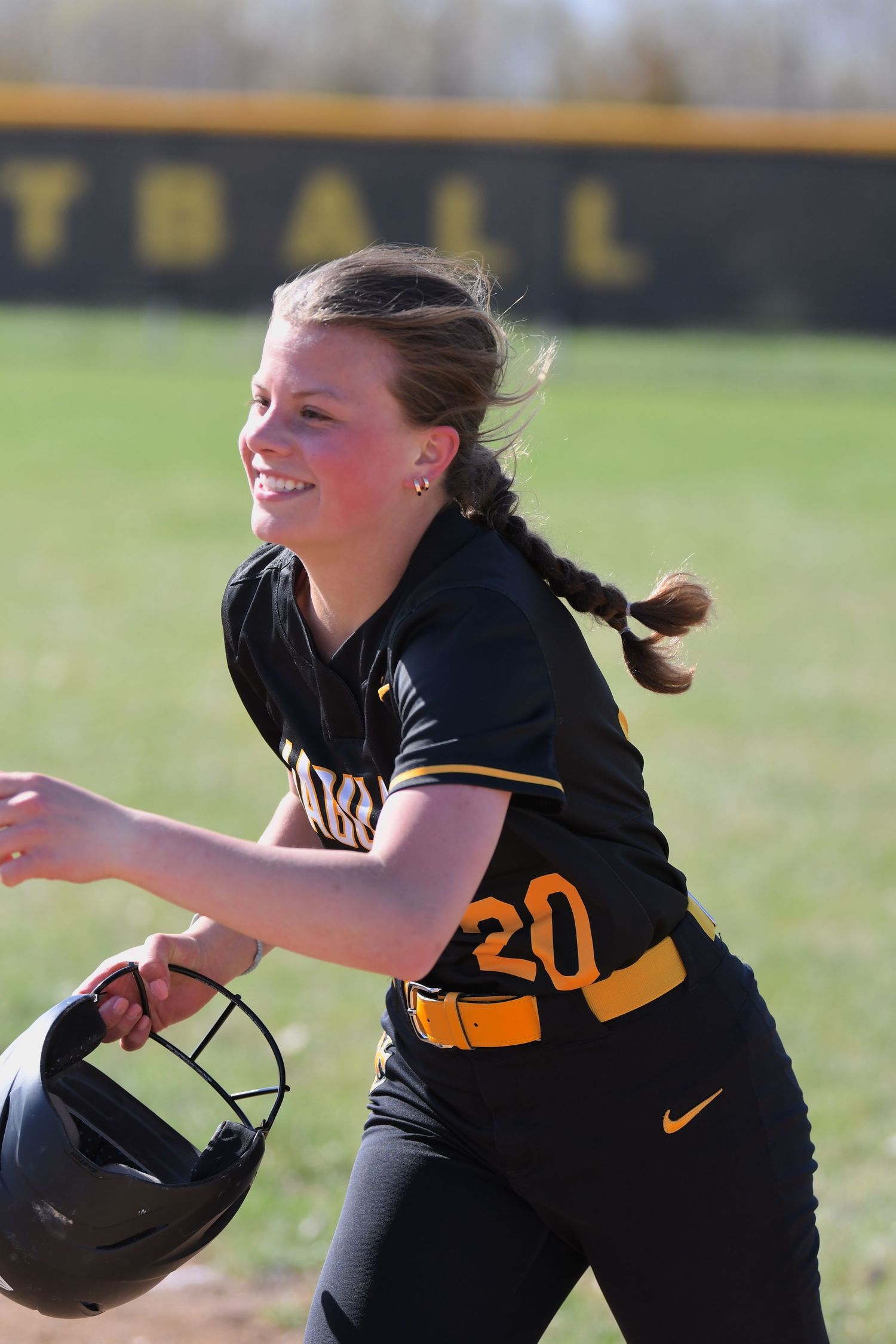 Player in black and gold uniform running to make defensive play on softball field.