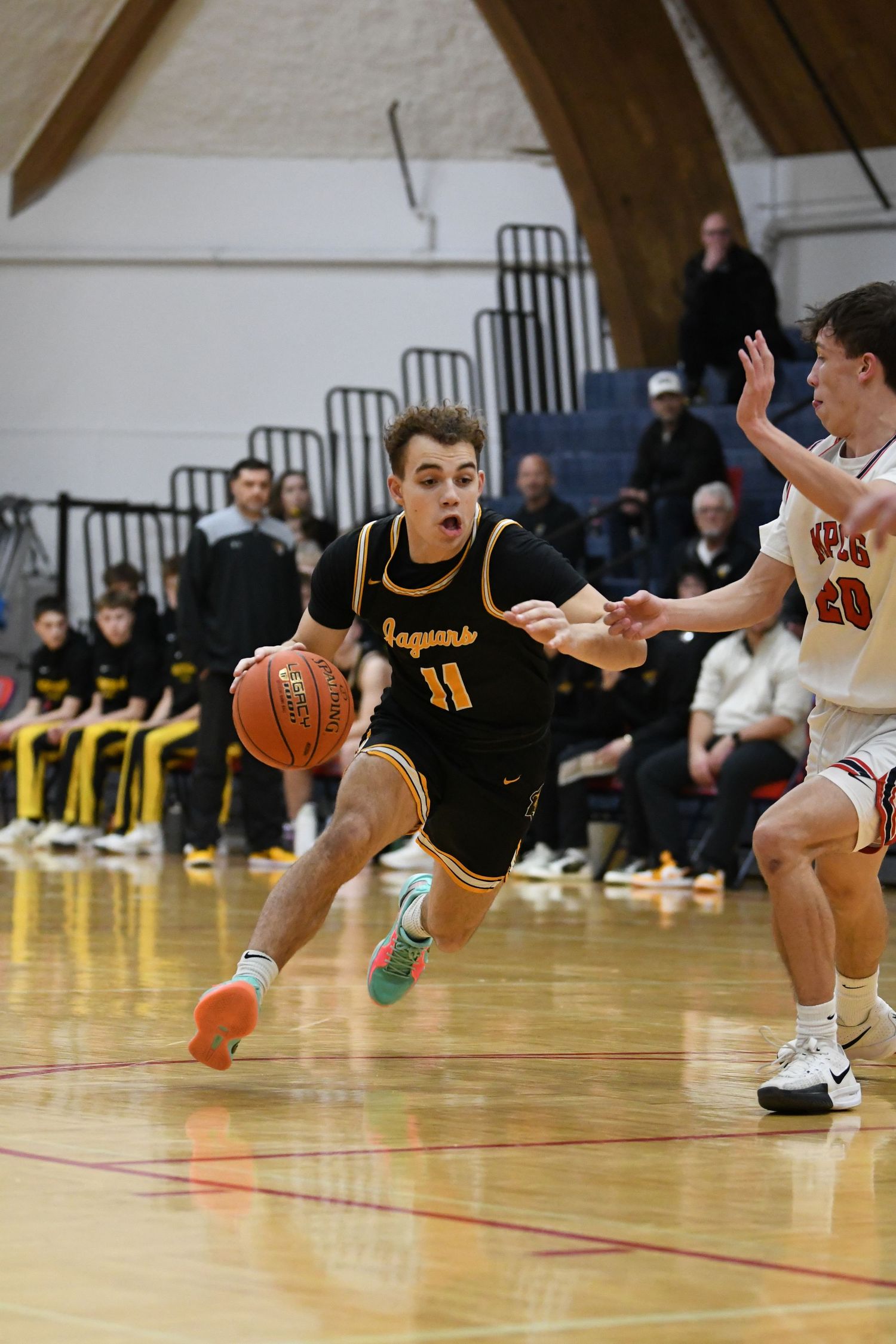 Player in black jersey dribbles basketball while driving past defender on court.