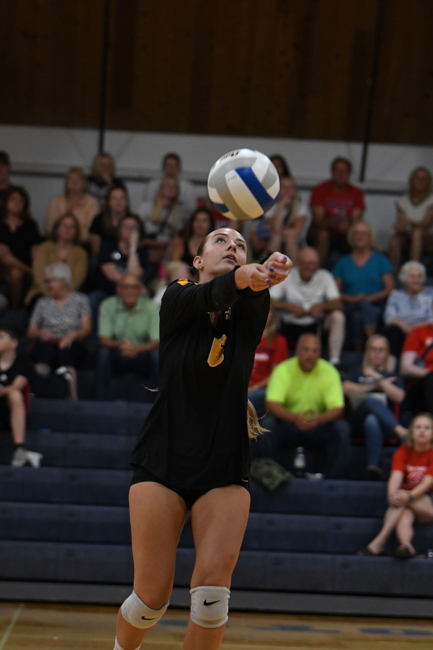 Volleyball player in black uniform dives to set the ball during a game.