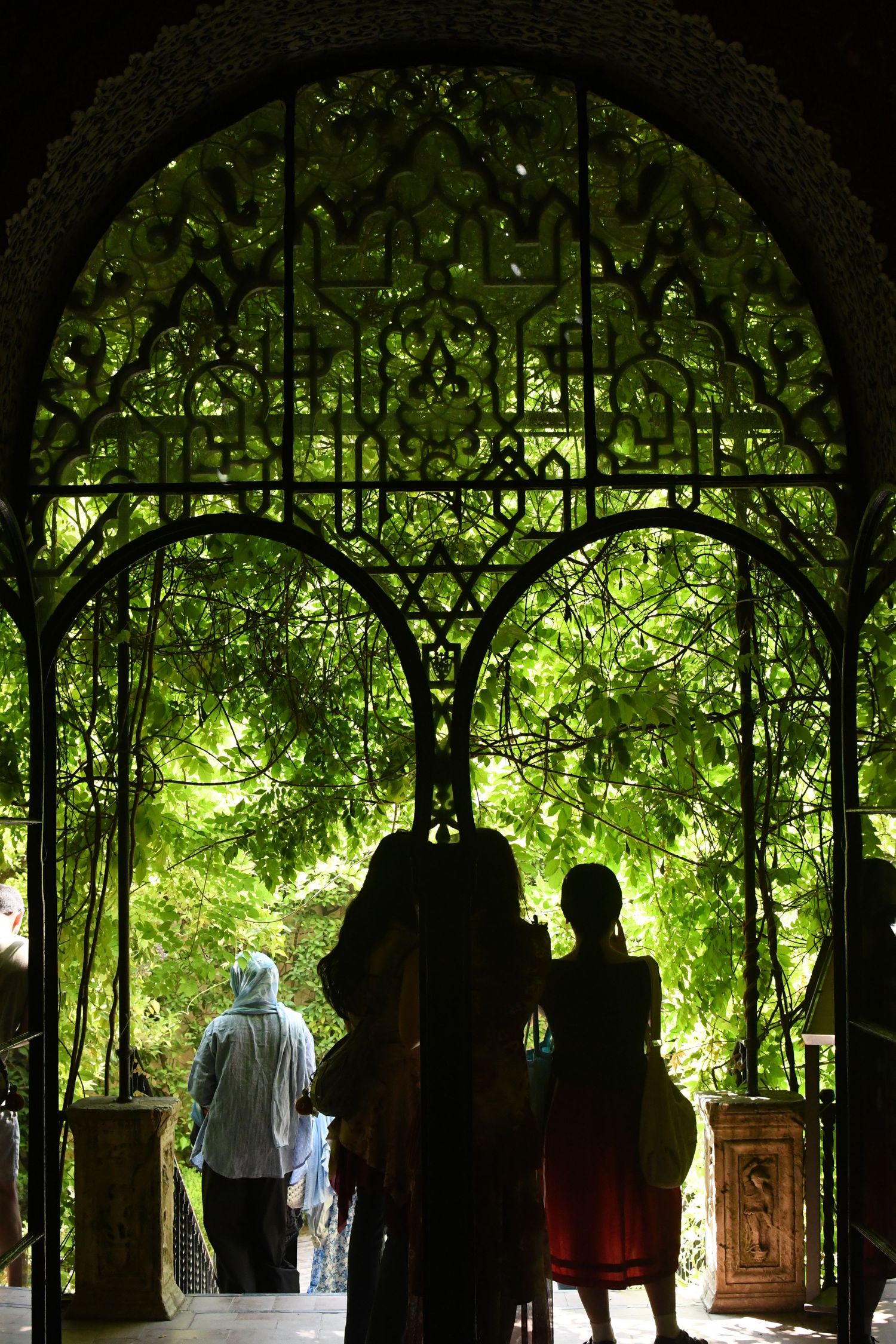 Silhouettes beneath an ornate archway surrounded by lush green foliage.