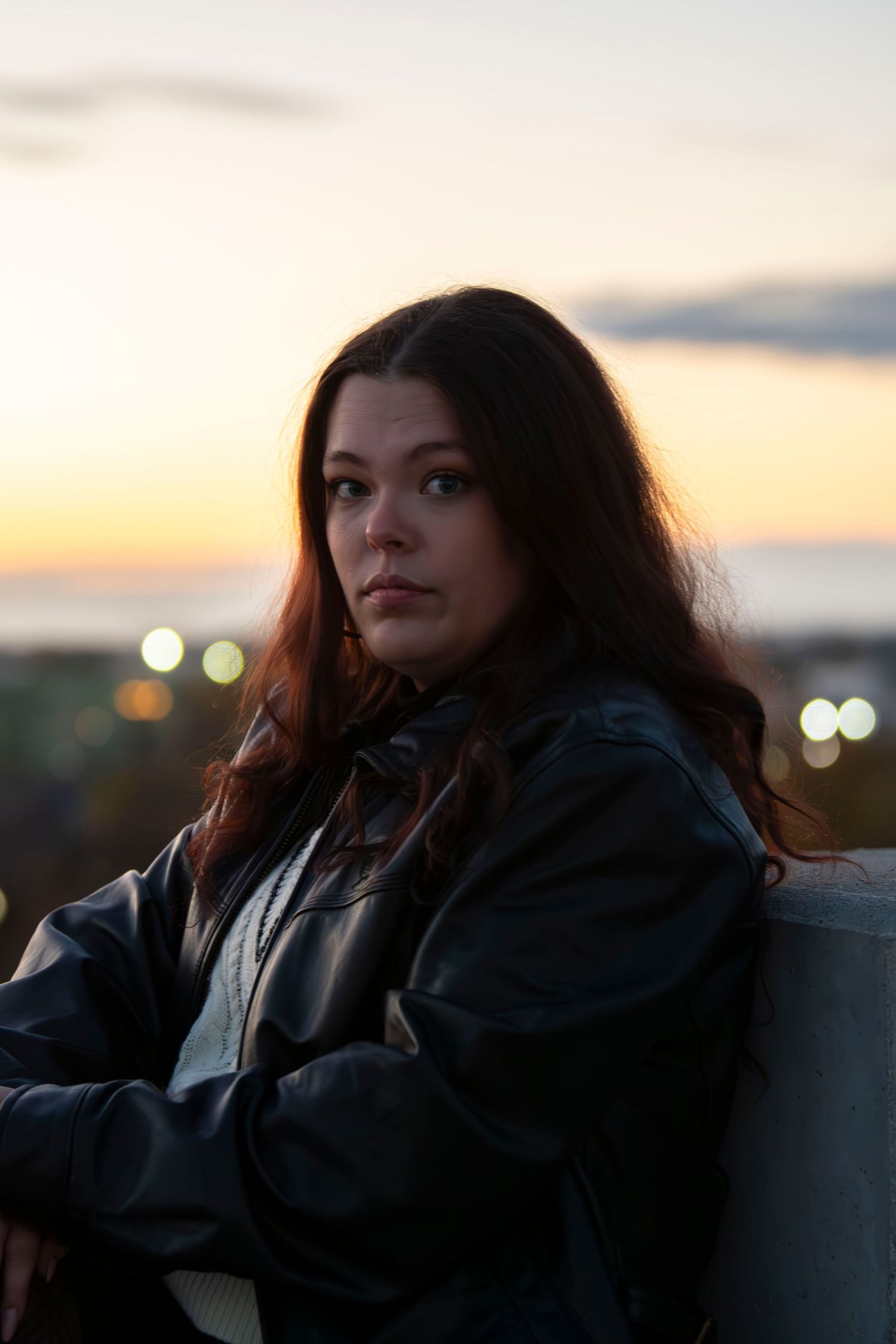 Silhouetted figure in a leather jacket gazes at a sunset cityscape during golden hour.