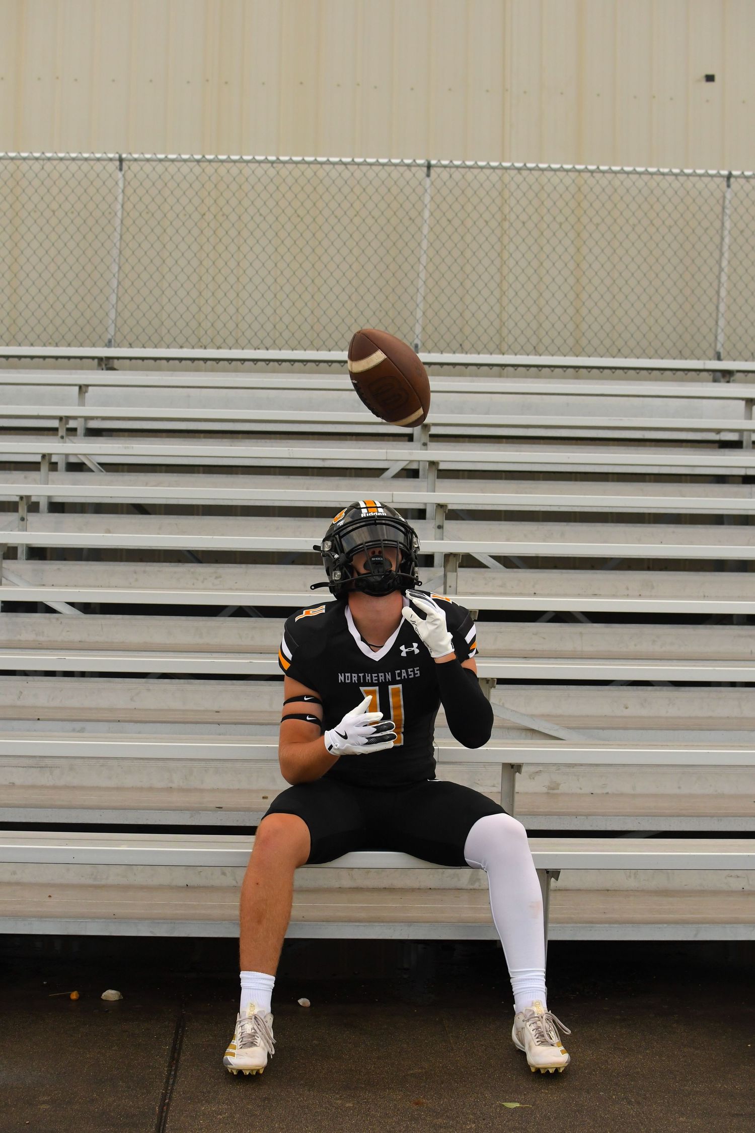 Football player in black uniform sits on bleachers catching a ball in sequential action shots.