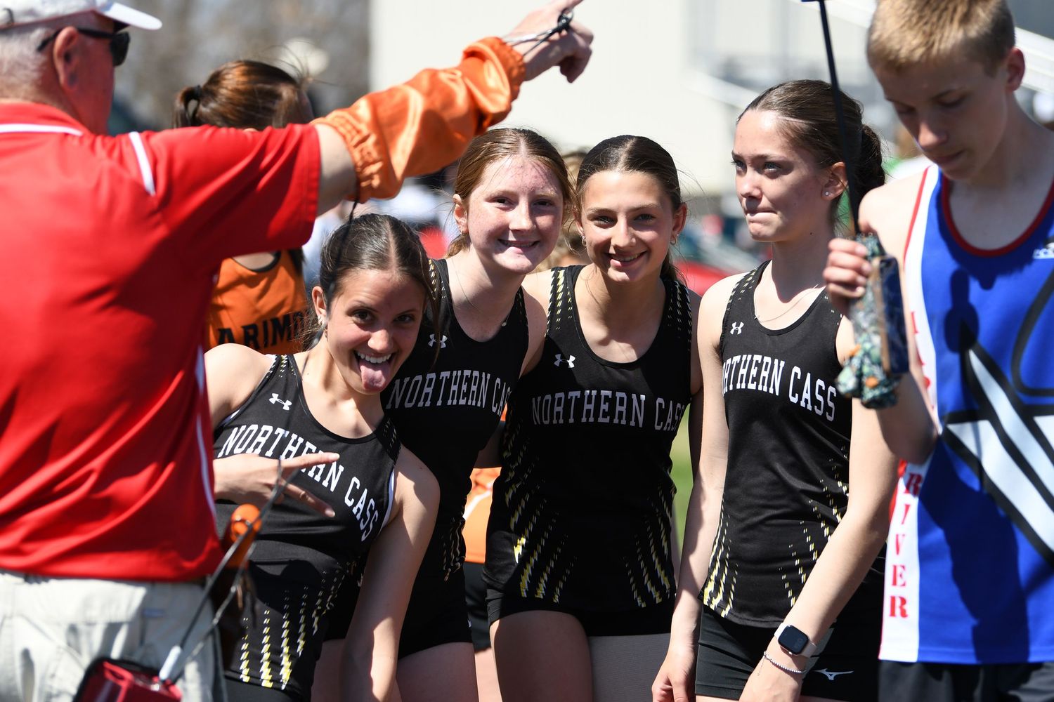 Track team members in black uniforms gather together during a sunny competition.