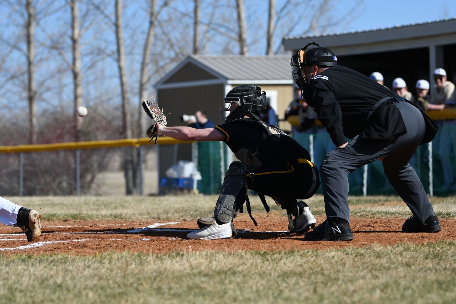 Baseball officials crouch behind home plate during game.
