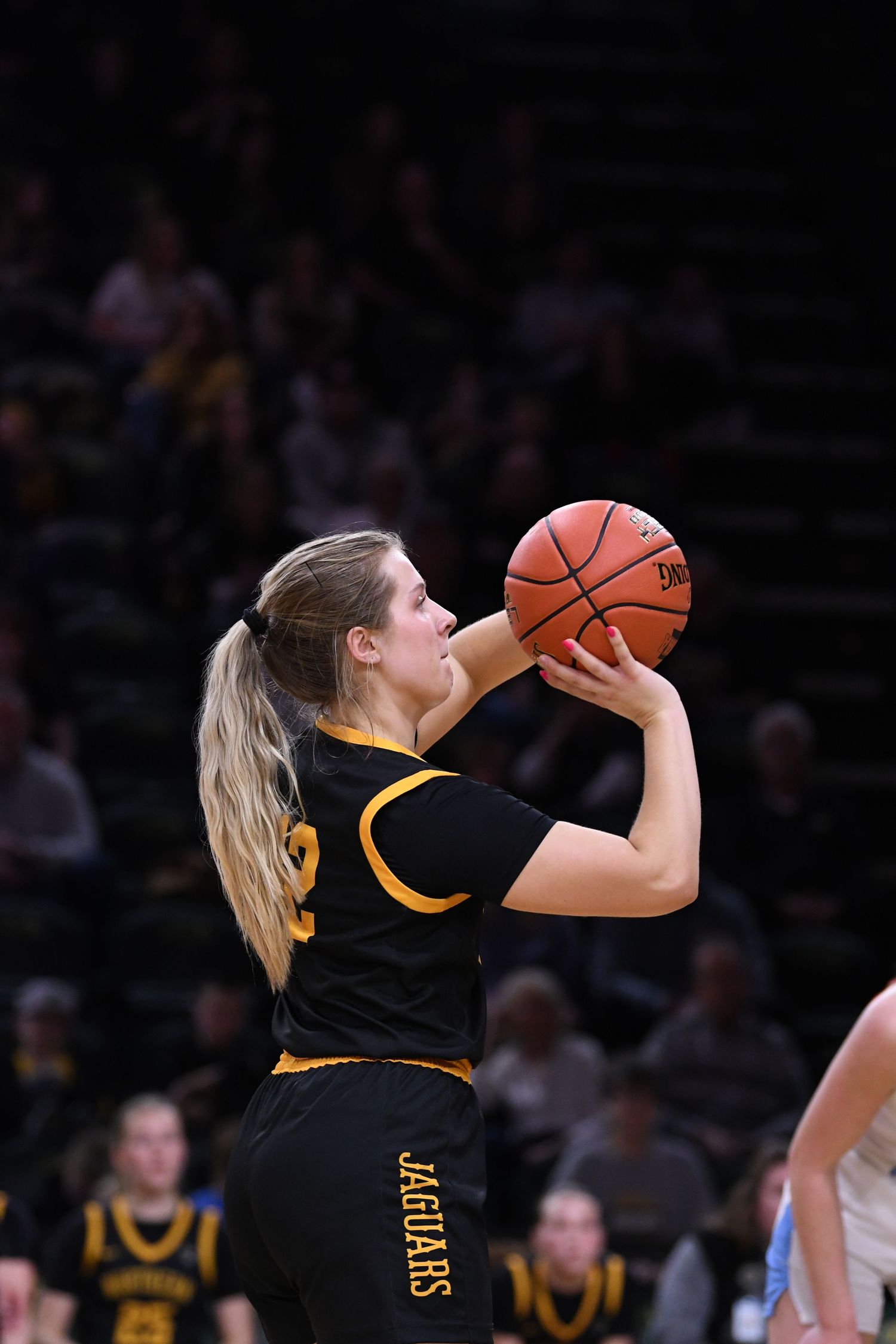 Player in black uniform takes shooting position during basketball game.