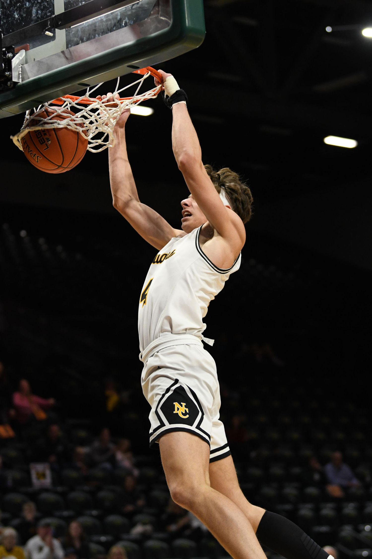 Basketball player performs powerful slam dunk during game in arena.
