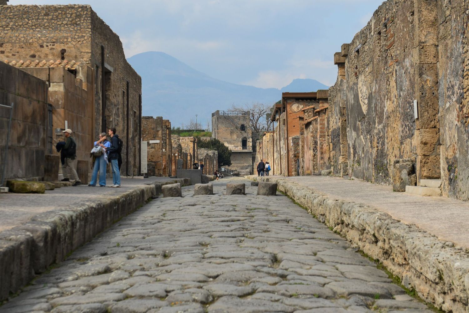 Ancient Roman stone street with preserved ruins and Mount Vesuvius in background at Pompeii.