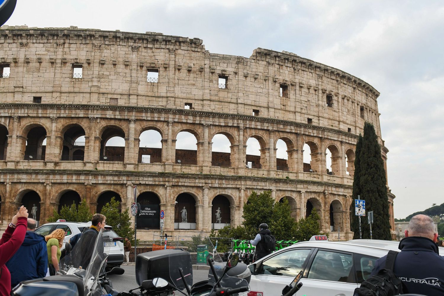 Exterior view of the Colosseum in Rome with parked vehicles in the foreground.