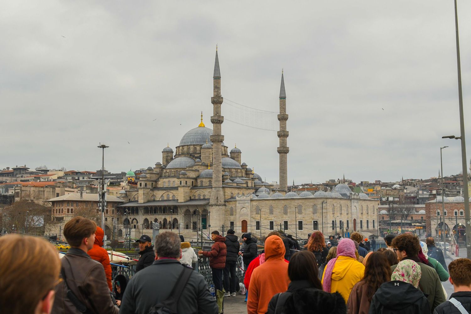 Tourists gather in front of the historic New Mosque (Yeni Cami) with its iconic minarets in Istanbul, Turkey.