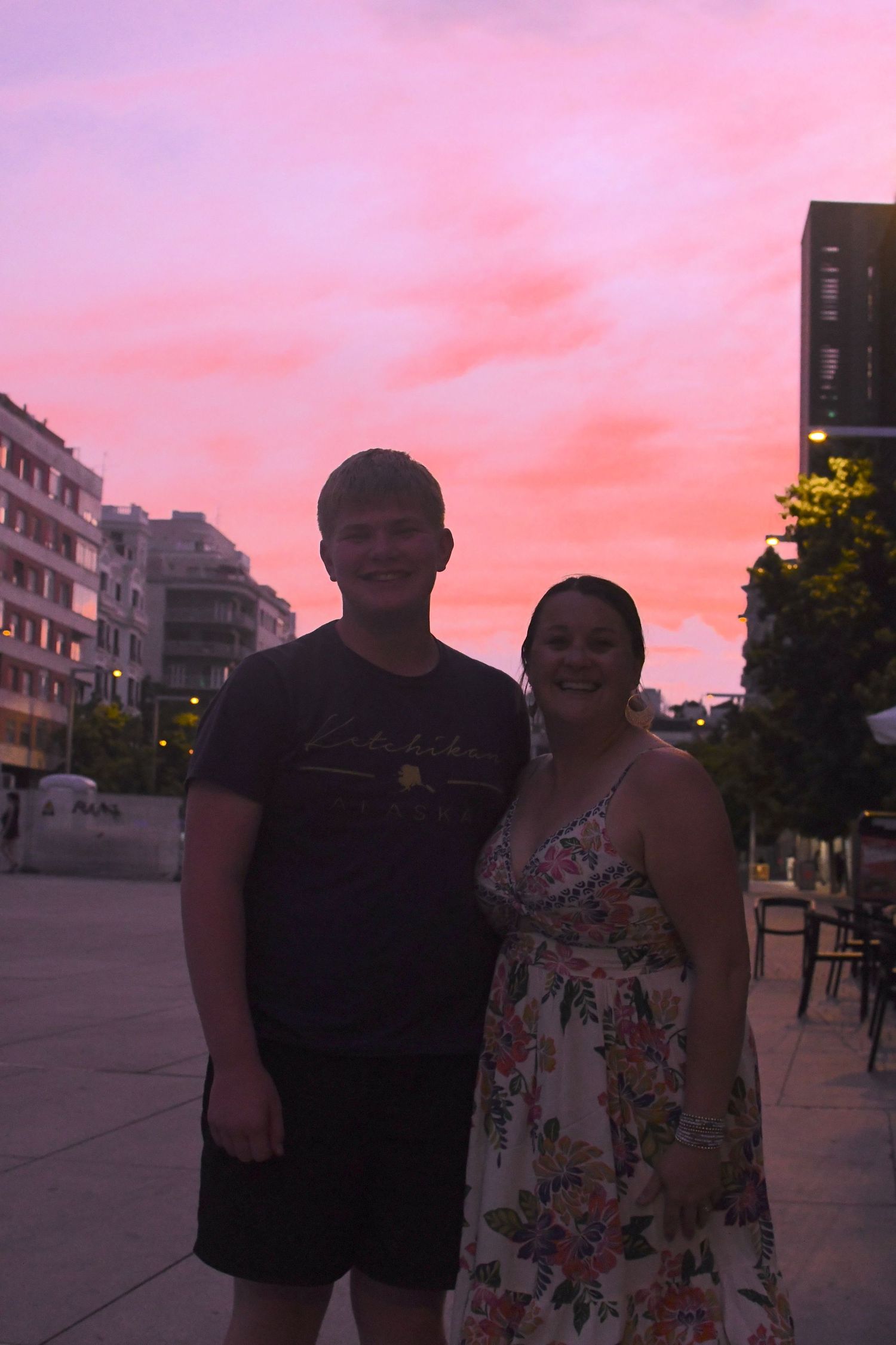Couple standing together against vibrant pink sunset sky in urban setting.