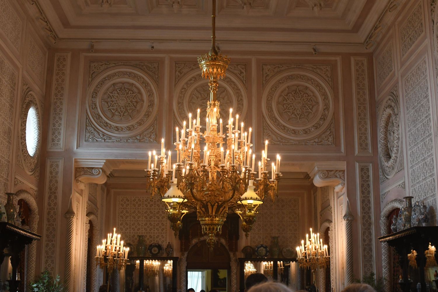 Ornate palace ballroom interior with crystal chandeliers and detailed white ceiling moldings.