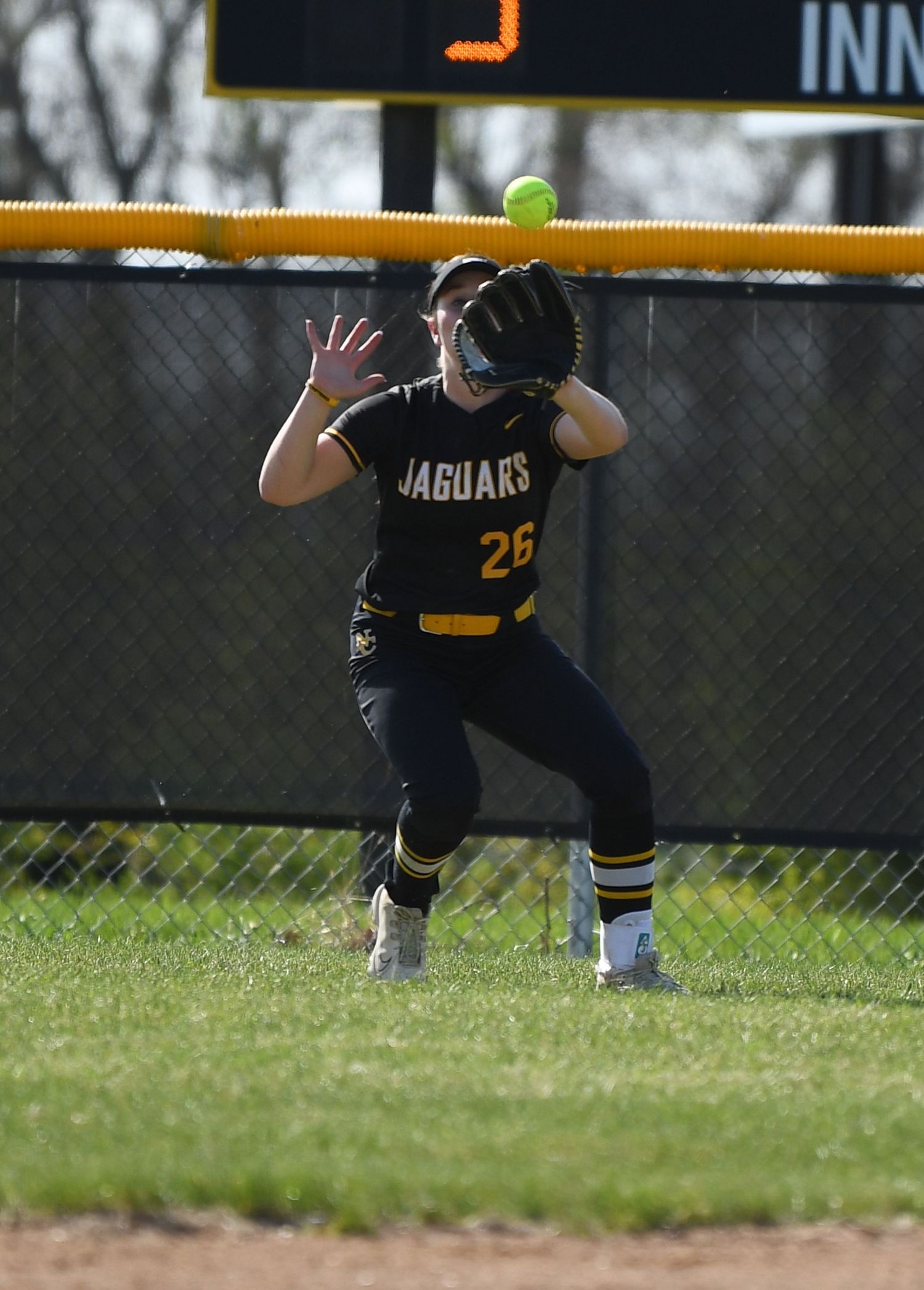 Softball fielder crouches in ready position on grass field during game.
