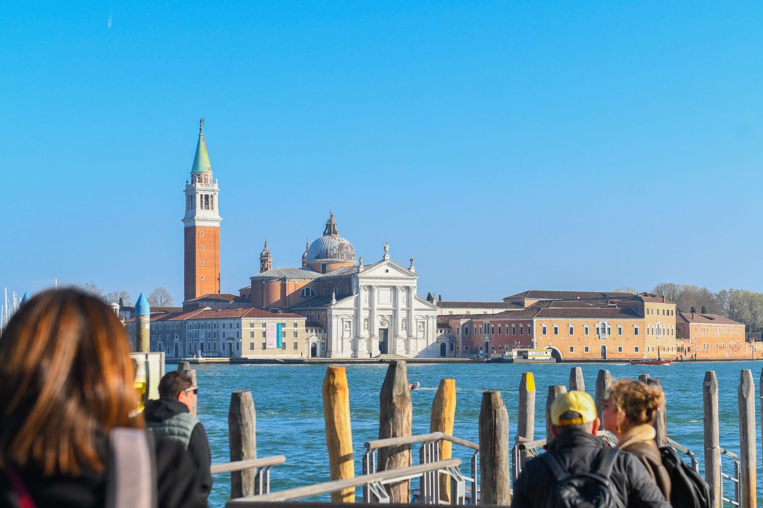 Venice skyline view across lagoon with San Giorgio Maggiore church and boats visible against blue sky.